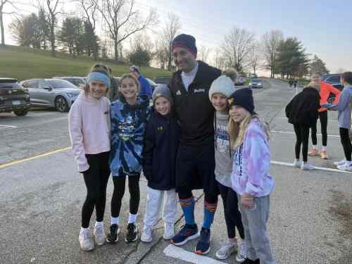 Group of children and an adult posing outdoors in a parking lot during winter.