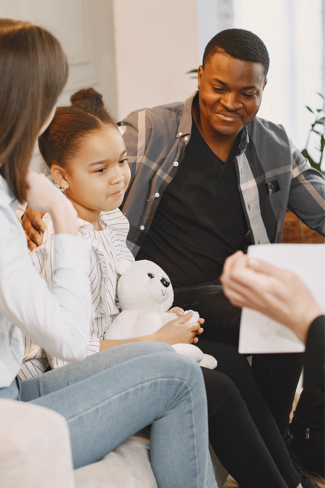 A group of people sitting together, with a man smiling and a young girl holding a stuffed polar bear, engaged in a conversation.