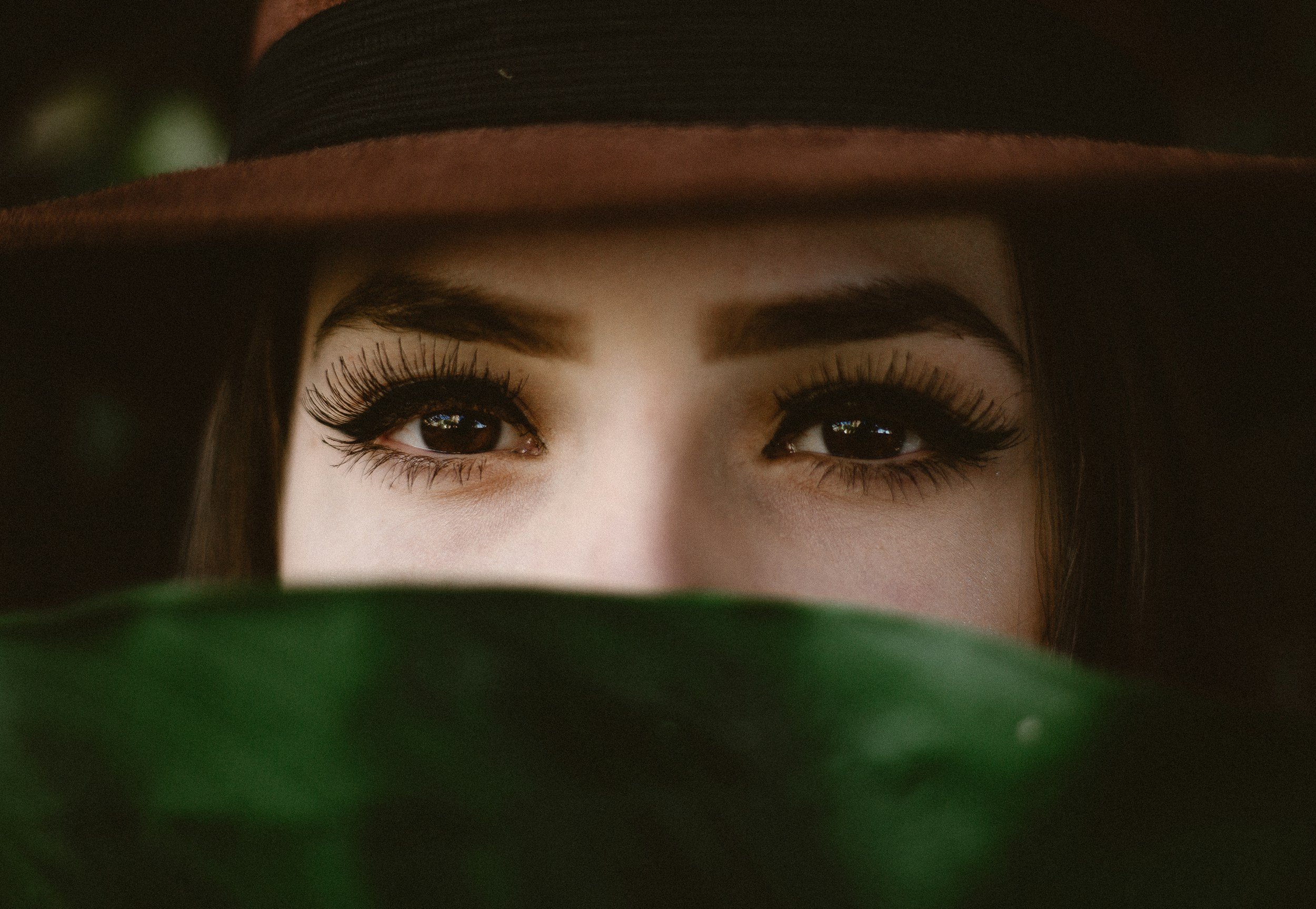 Close-up of a woman's eyes with dark makeup, partially obscured by a green object in the foreground.
