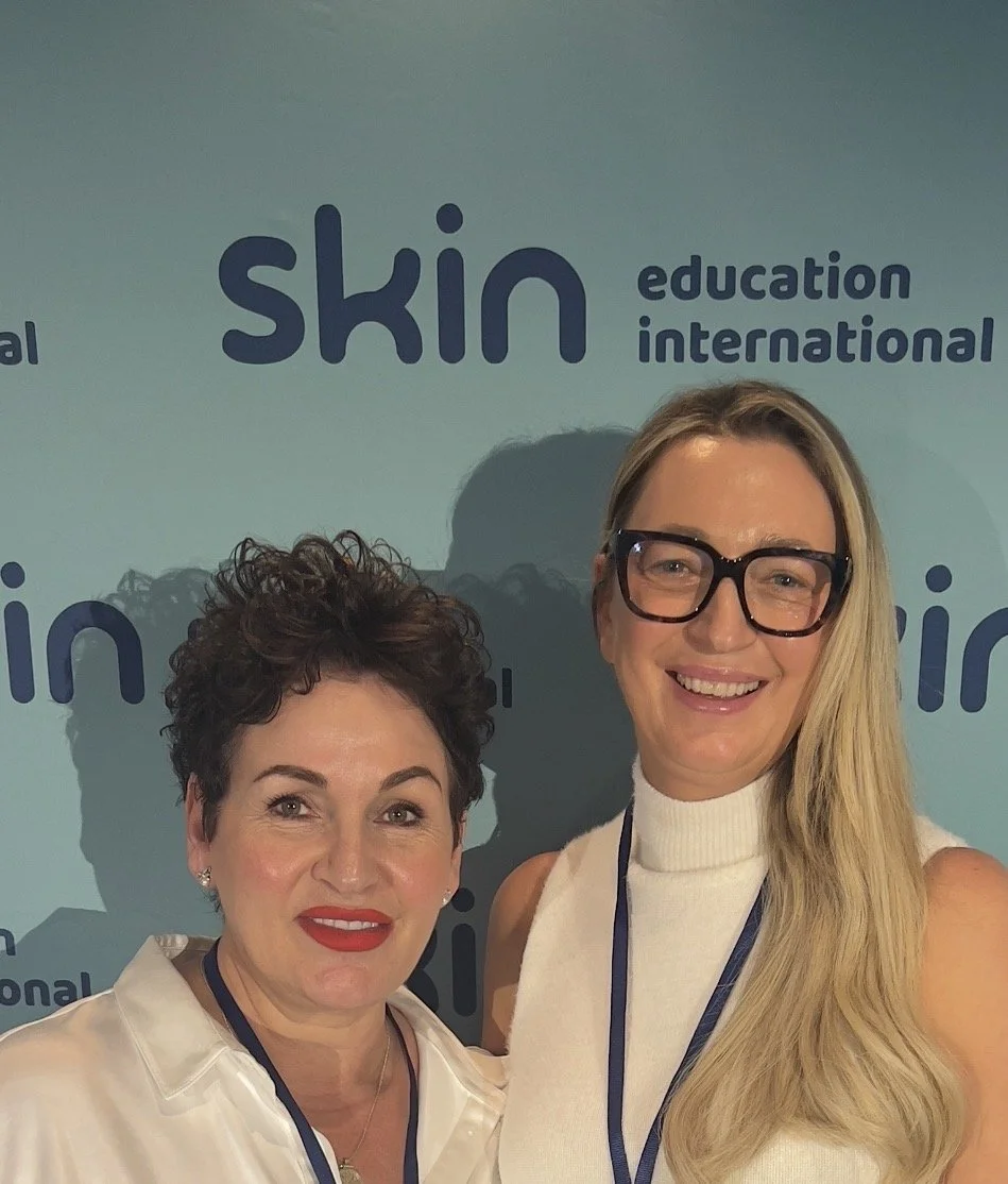 Two women smiling and posing for a photo at an event with a backdrop that has the words 'skin' and 'education international' visible.