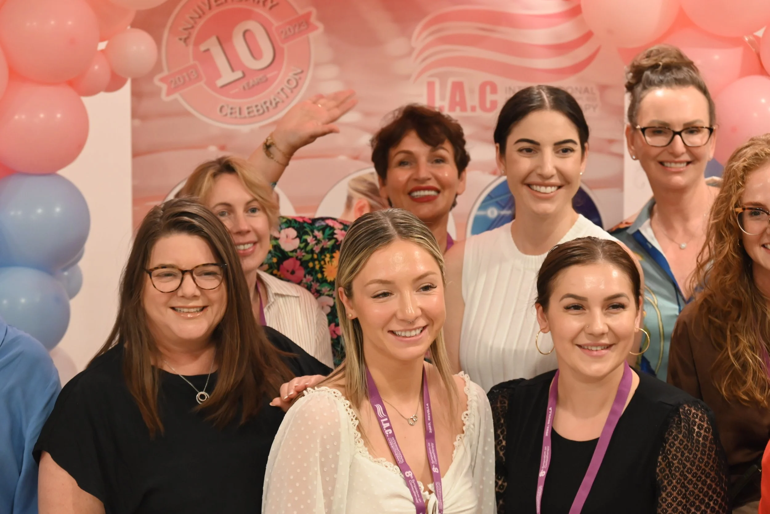 Group of women celebrating at an event with pink and blue balloons, and a backdrop that has a 10th anniversary celebration logo.