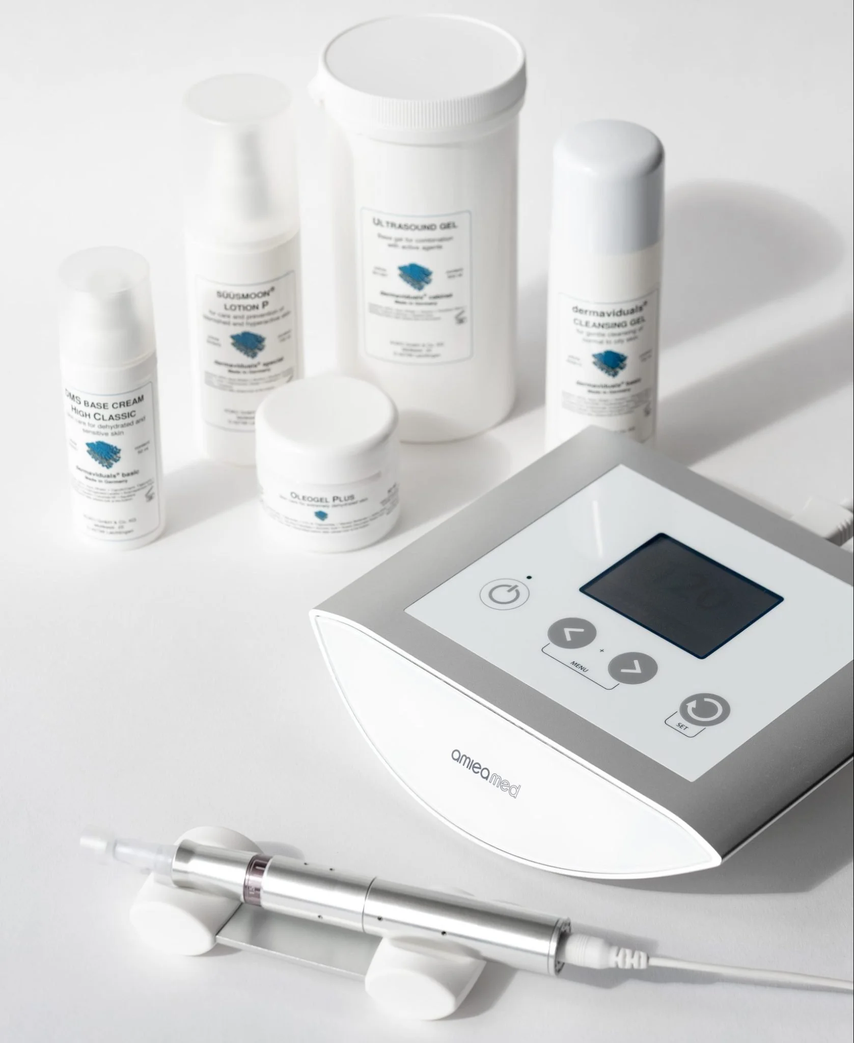 Medical testing equipment including a digital ultrasound gel warmer, bottles of ultrasound gel, a syringe, and a digital control device with a display screen and buttons on a white surface.