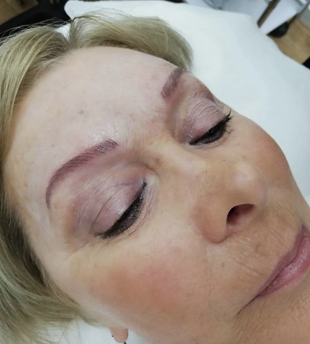 Close-up of a woman lying down with her eyes closed, showing freshly done eyebrow and eyelash treatments.