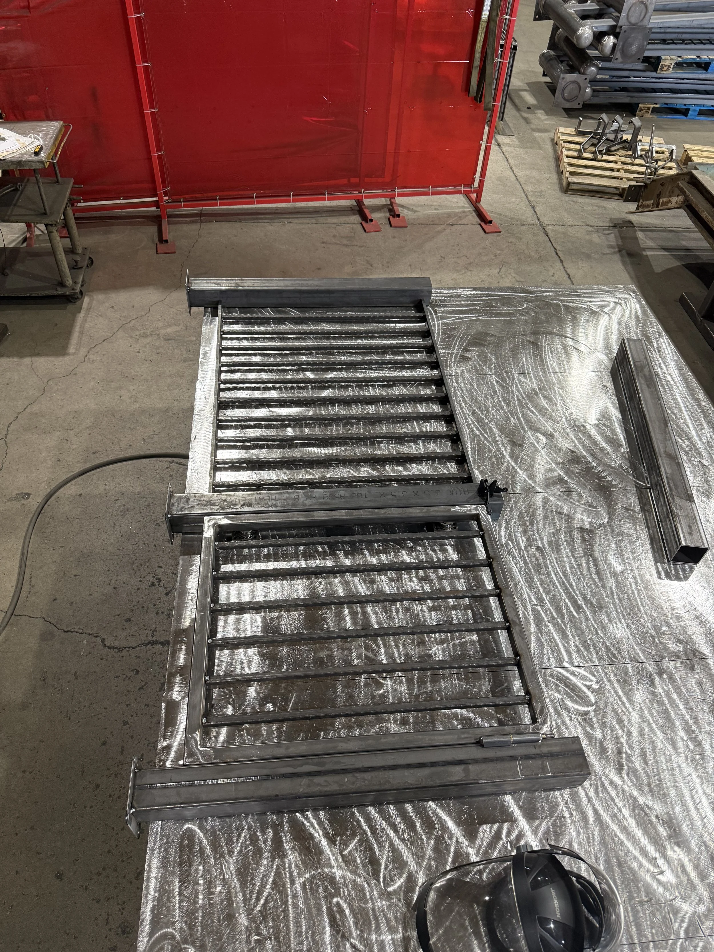 Metal roller conveyor on a work table with a black safety helmet on the floor nearby, in an industrial warehouse setting.