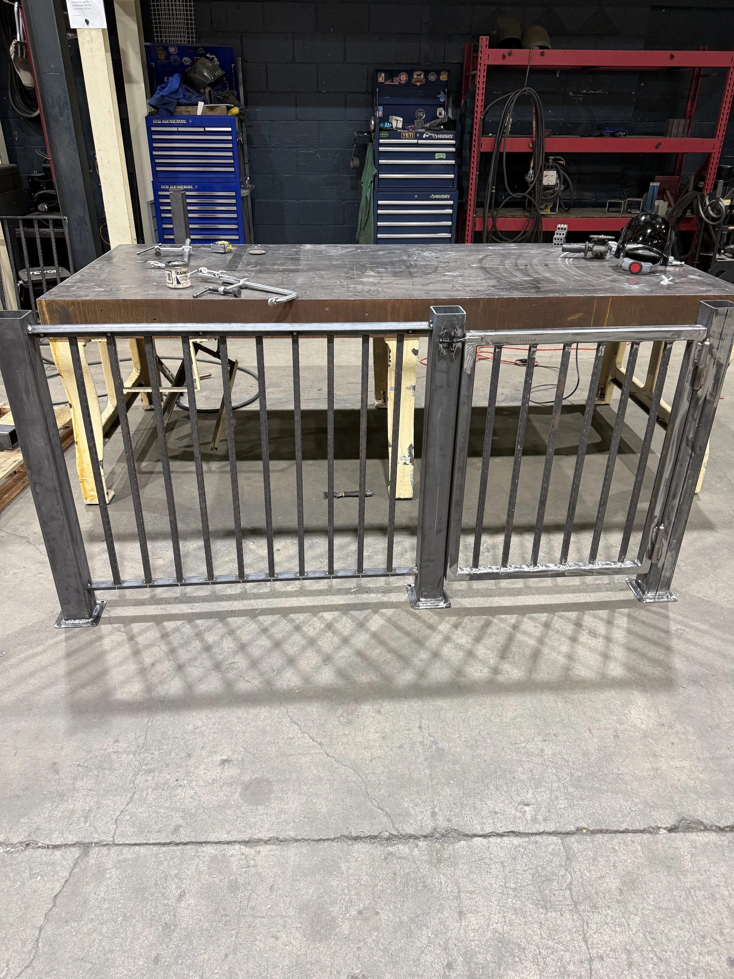 A metal workbench with various tools and equipment on top, surrounded by a metal safety fence in an industrial workshop.