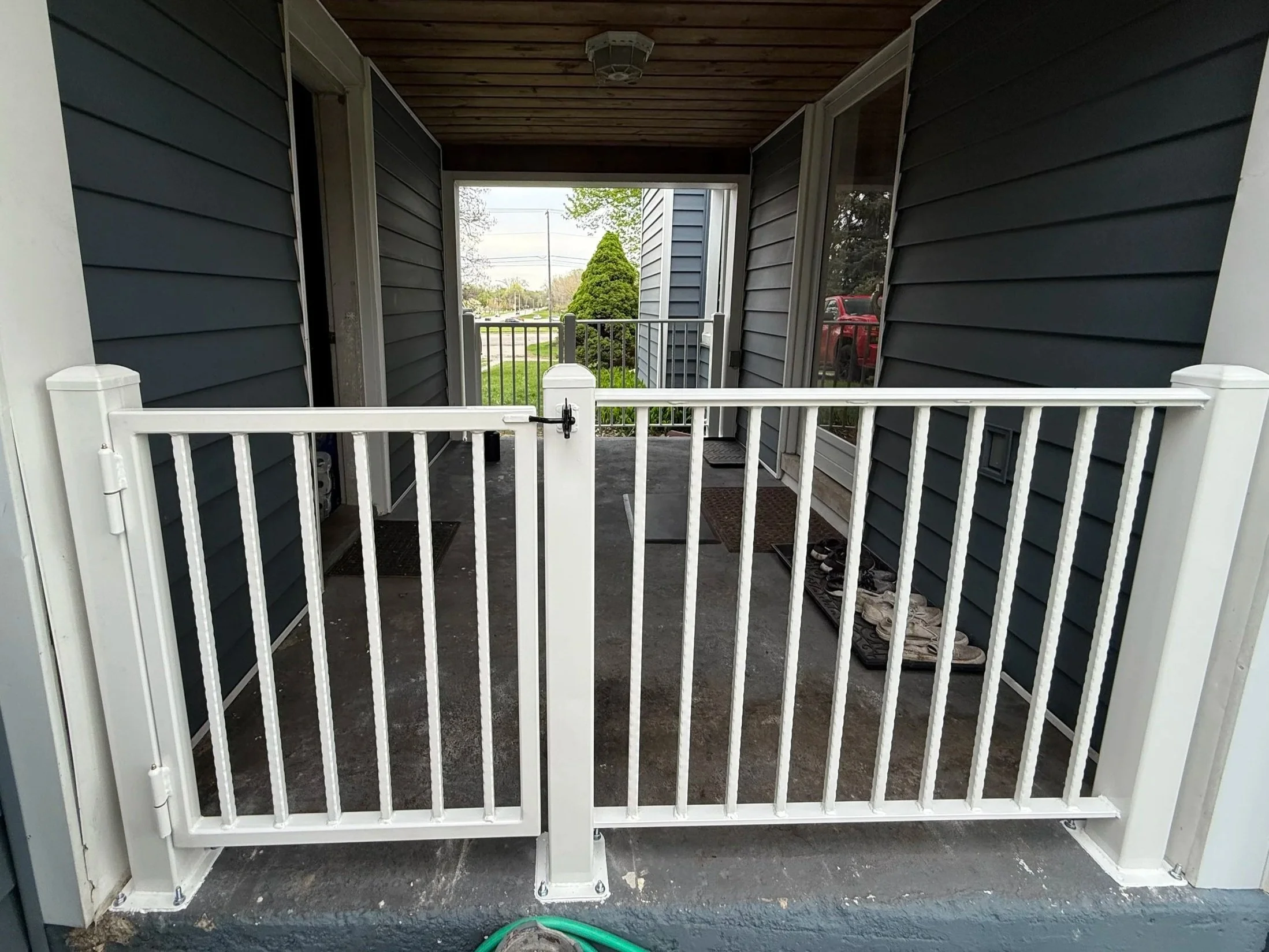 Image of a front porch with a white security gate and a view of a tree, sidewalk, and parked car outside.