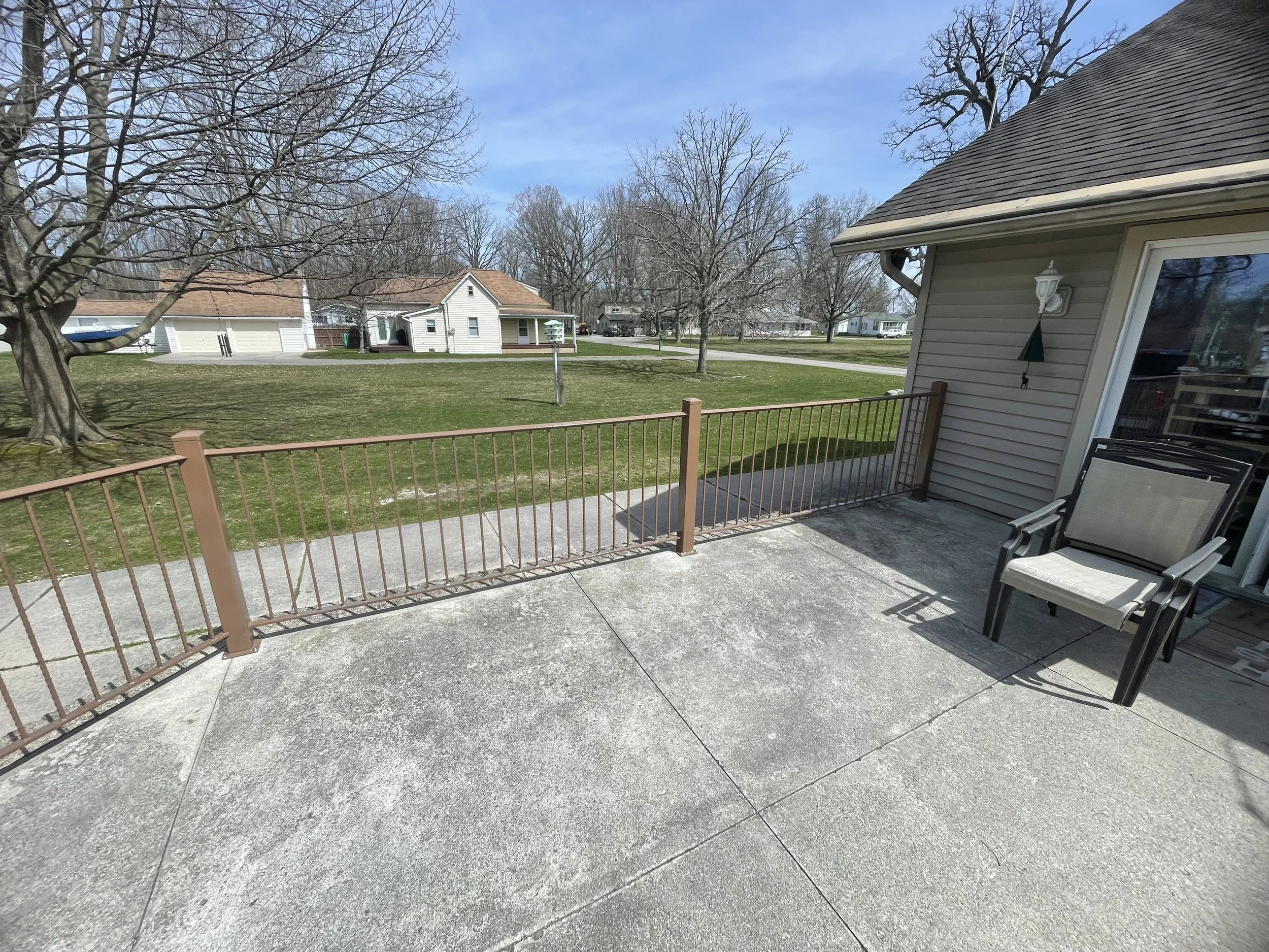 A backyard patio with lawn, trees, neighbor houses, and a sky with some clouds.