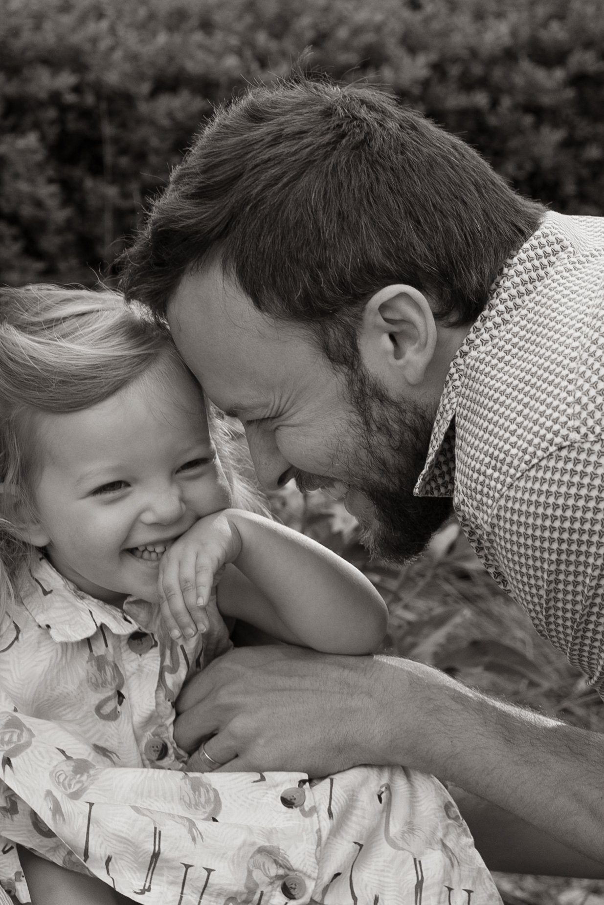 A man and young girl sharing a joyful moment outdoors, with their foreheads touching and smiling.
