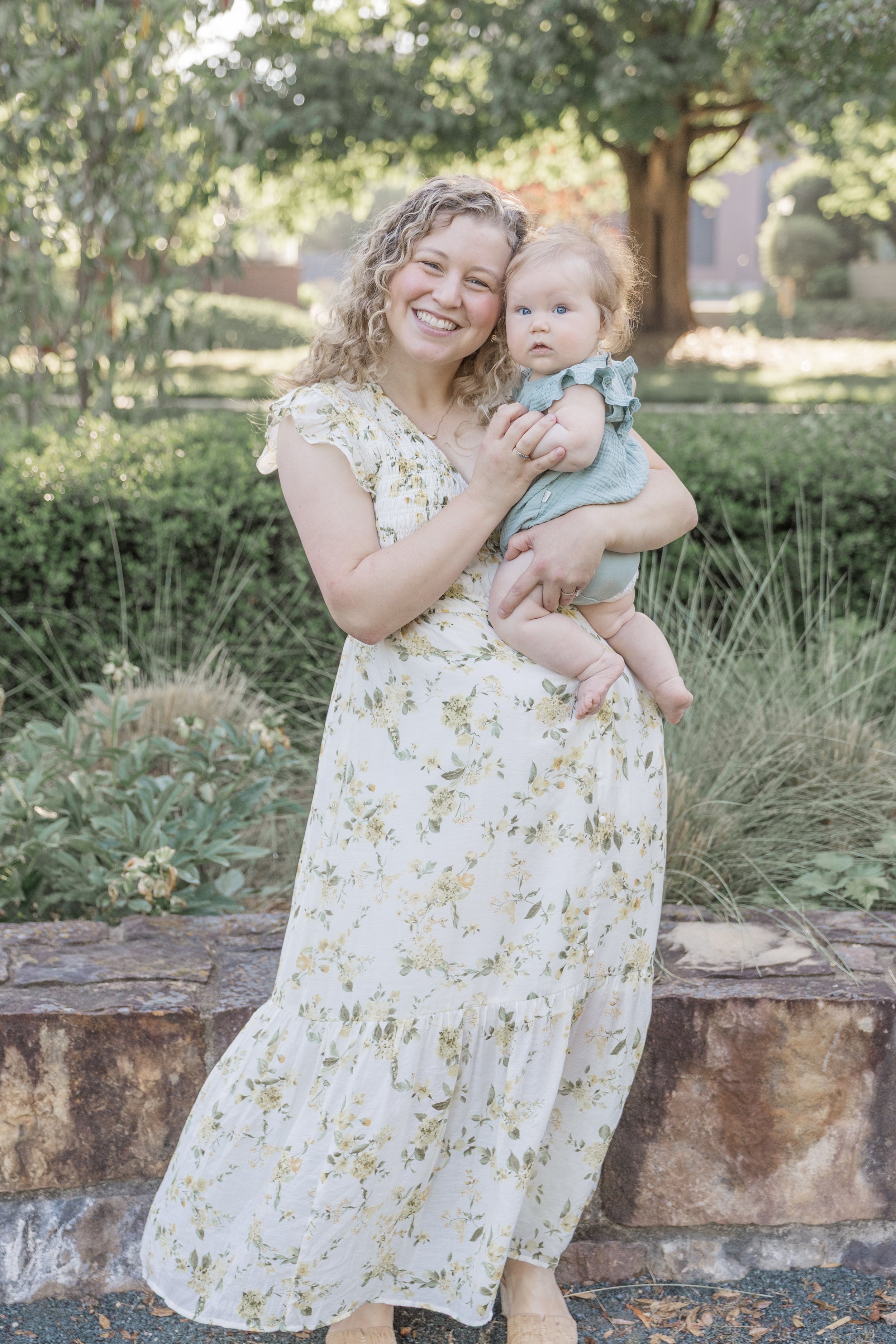 A woman in a floral dress holding a toddler girl in a park.