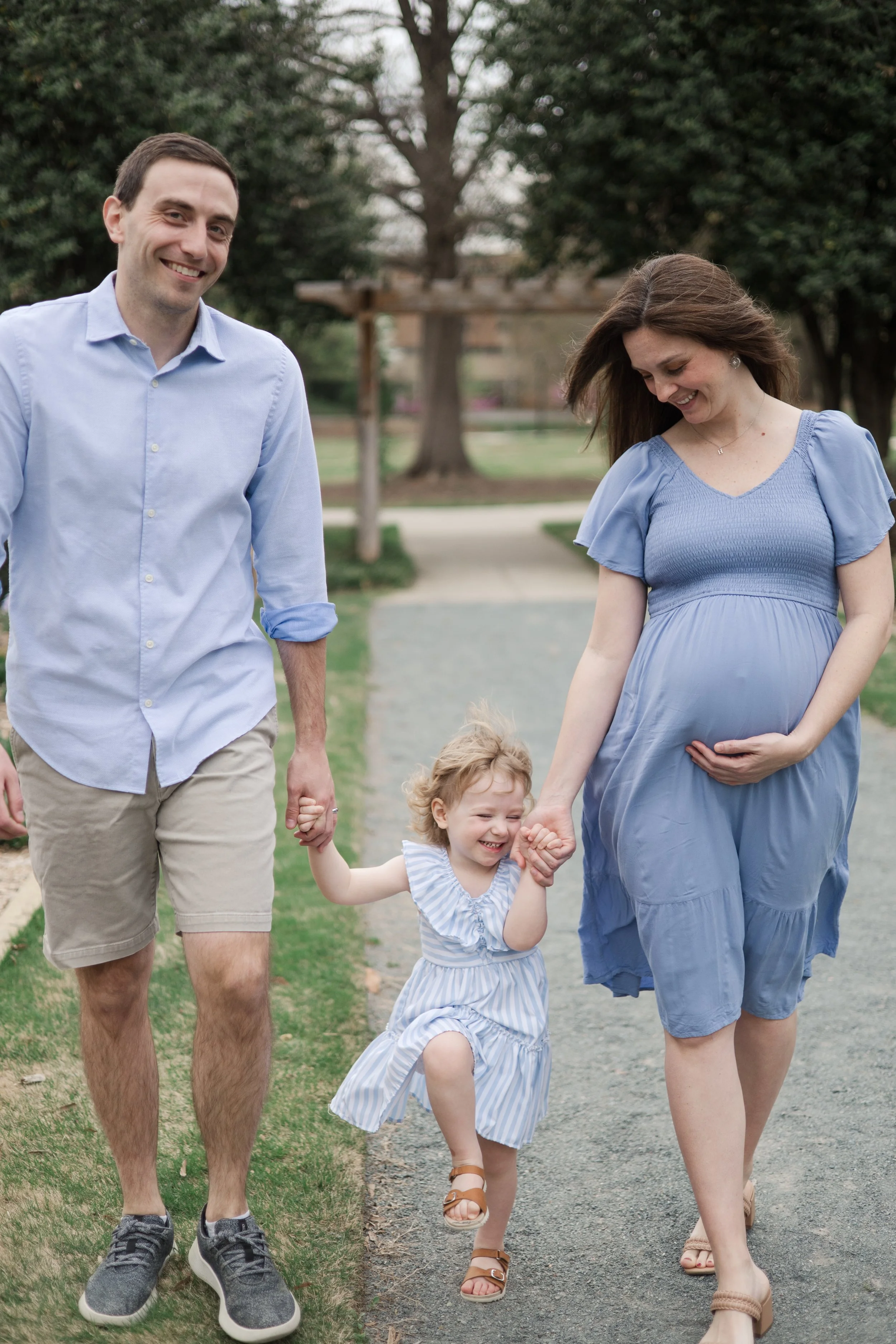Pregnant Mother holding hands with Toddler Daughter while embracing Belly during Maternity Photoshoot