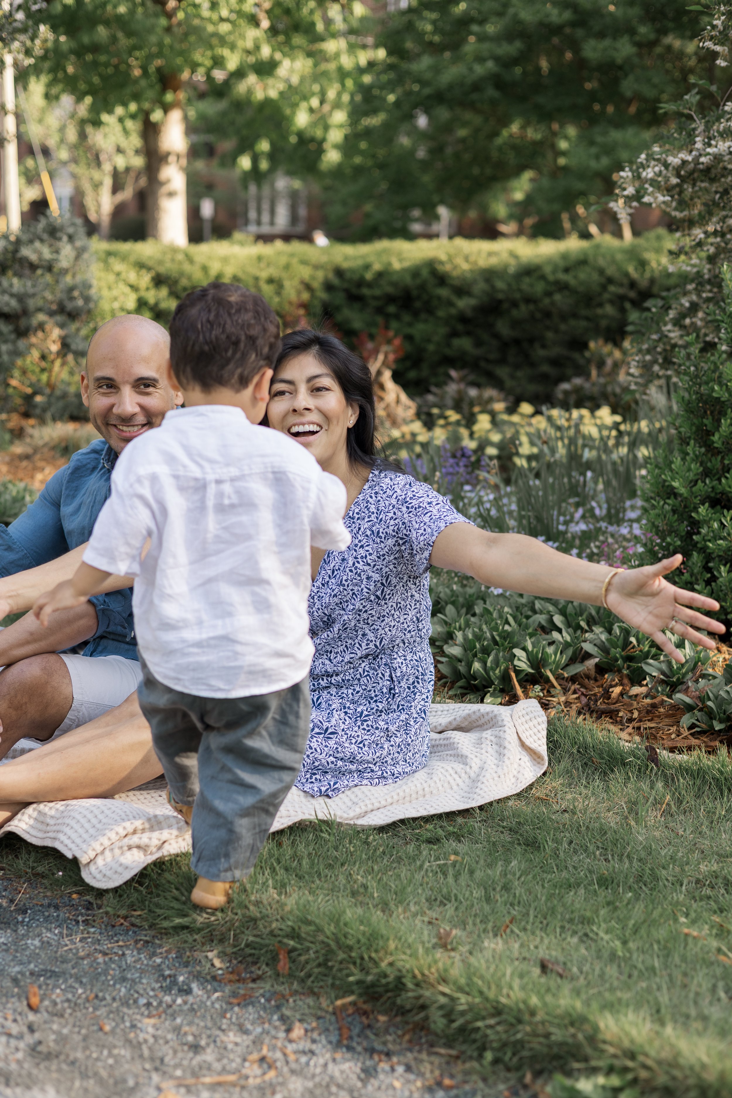 A joyful family enjoying a picnic outdoors in a garden, with a woman, a man, and a young boy in the scene.