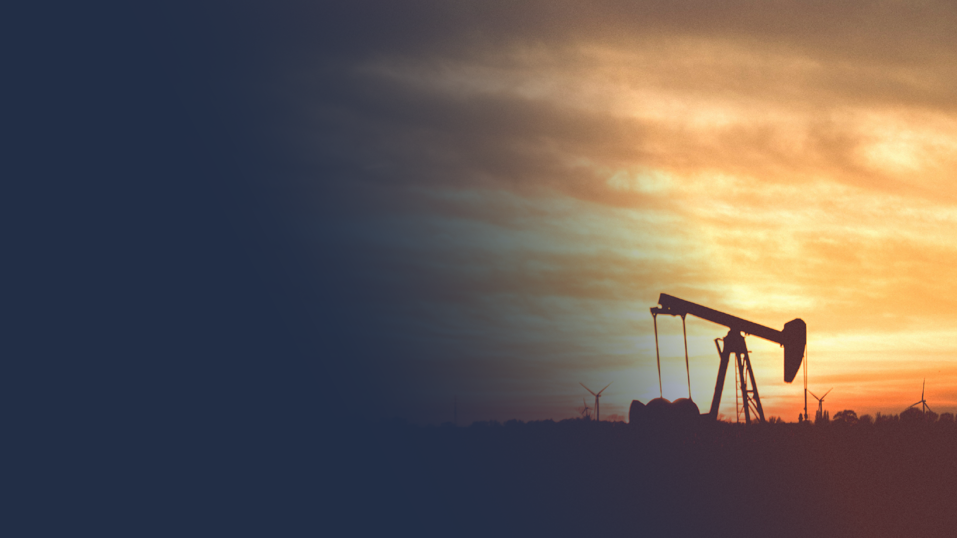 Silhouette of an oil pumpjack against a sunset sky with wind turbines in the background.