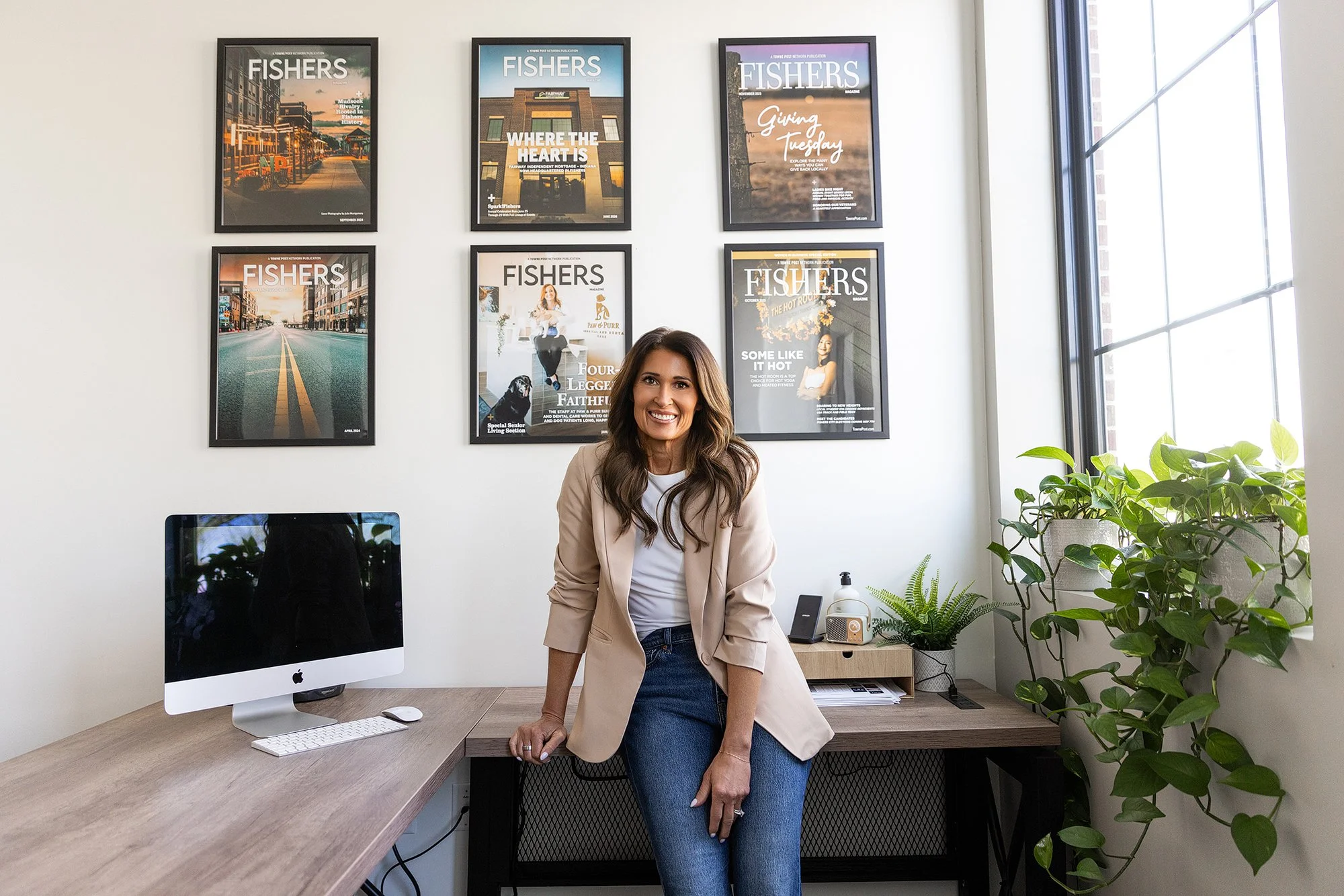 Woman sitting on her desk in a home office with framed Fishers magazine covers, environmental branding photo in Fishers, IN