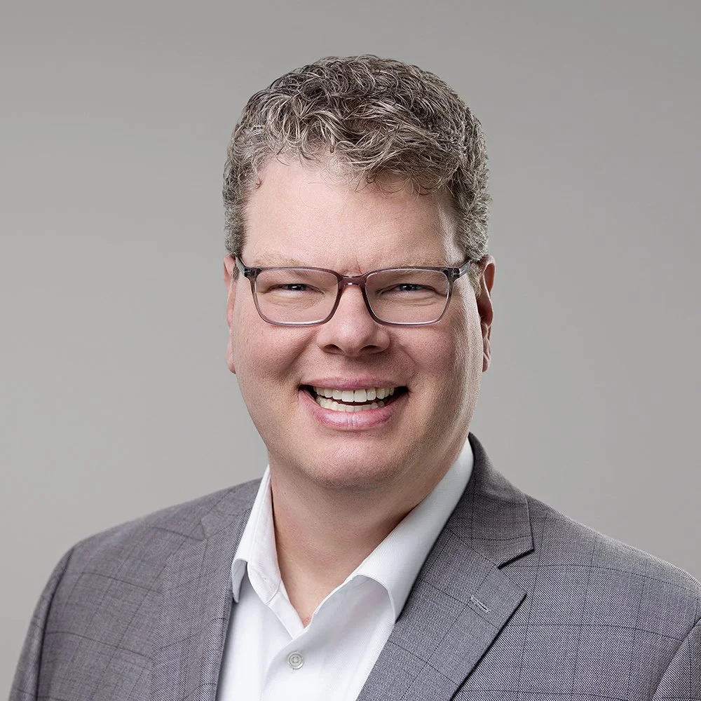 Eric Young smiling in glasses and a gray blazer, business headshot by Square Mouth Studios