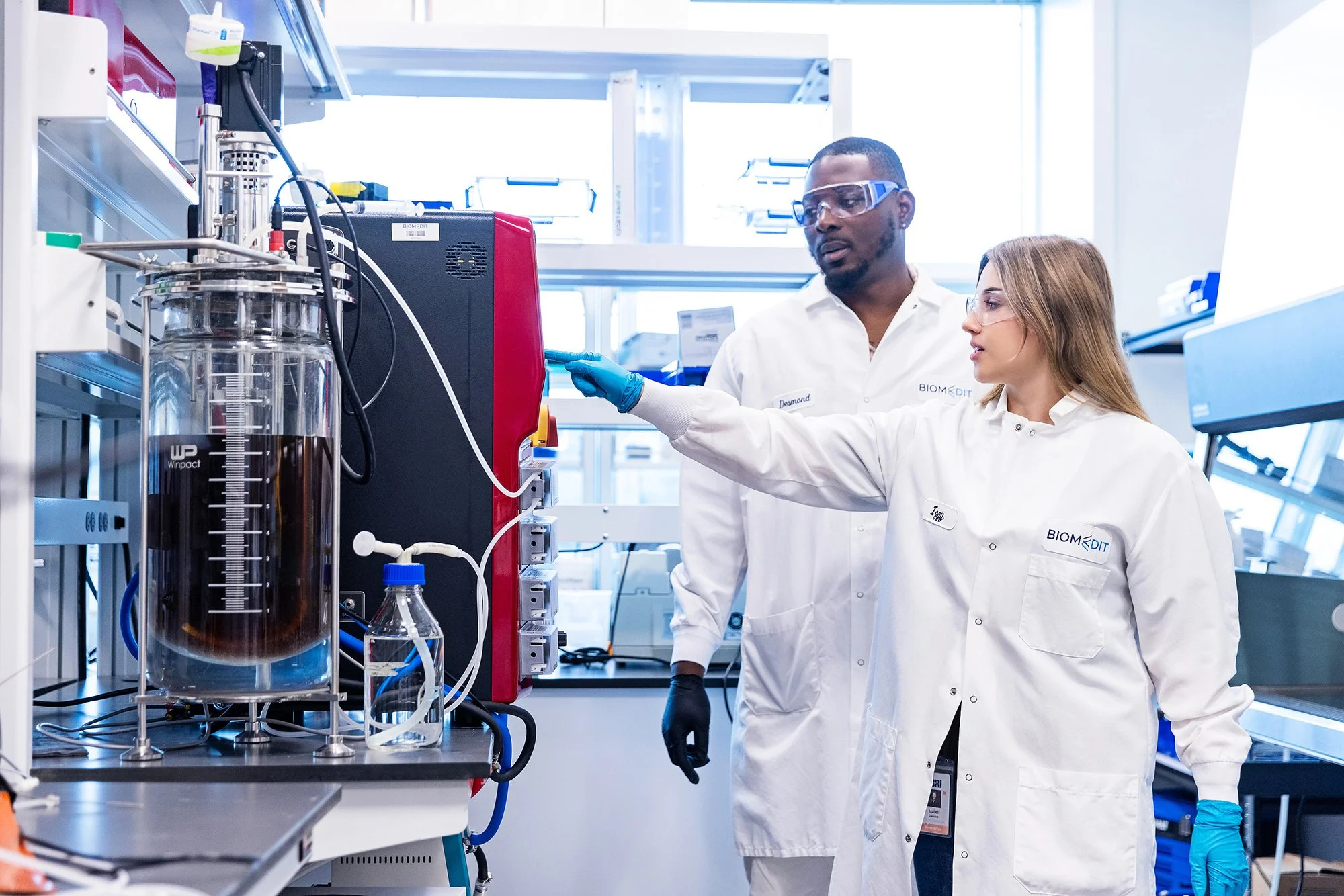 Two scientists in lab coats inspecting a bioreactor, BiomEdit laboratory brand photography