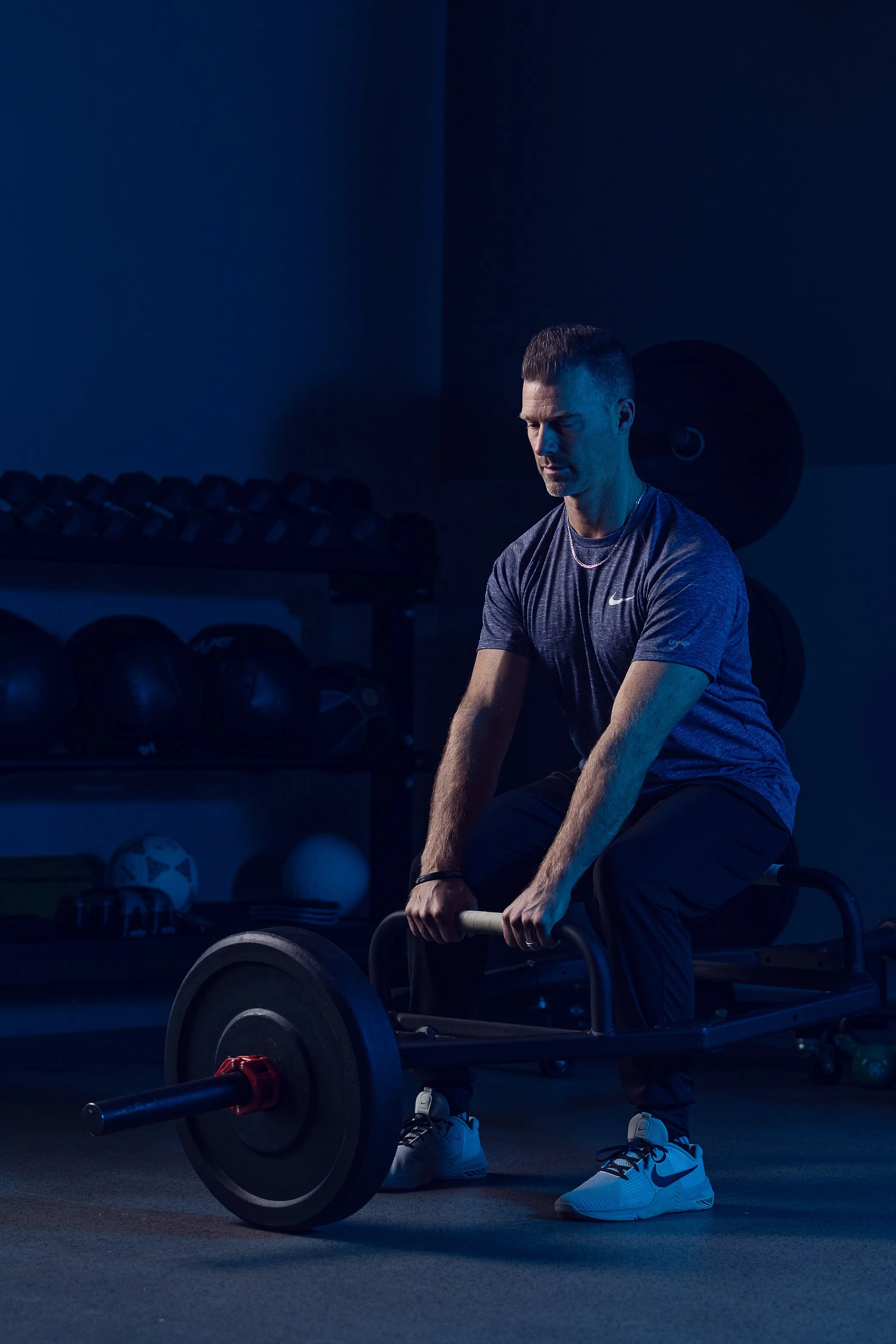 Physical therapist lifting a barbell in a dark, dramatically lit gym, Indianapolis fitness branding photo