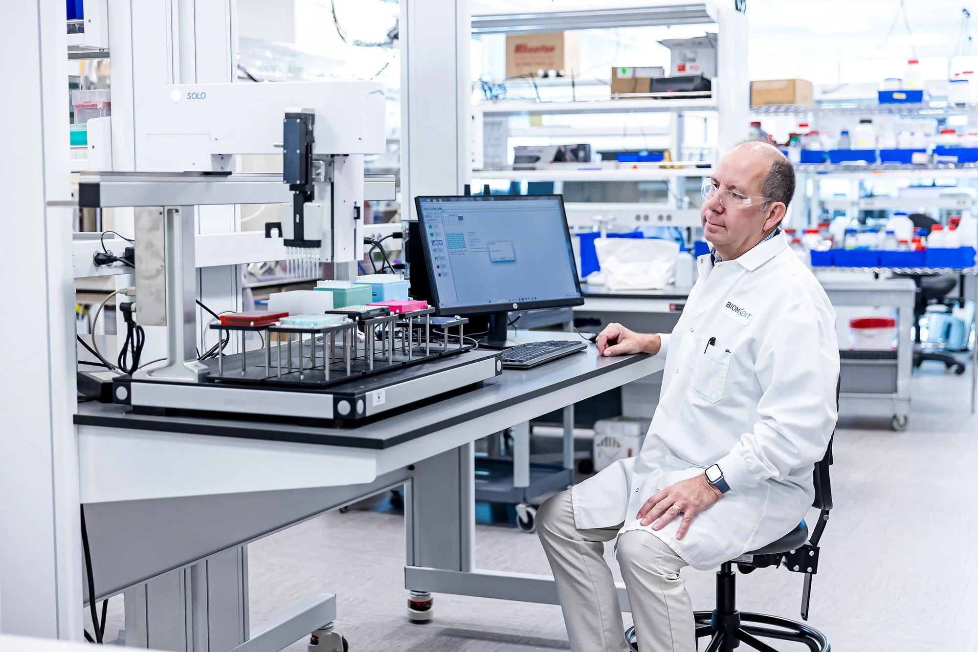Scientist in a lab coat seated at a workstation in a modern laboratory, BiomEdit brand photography