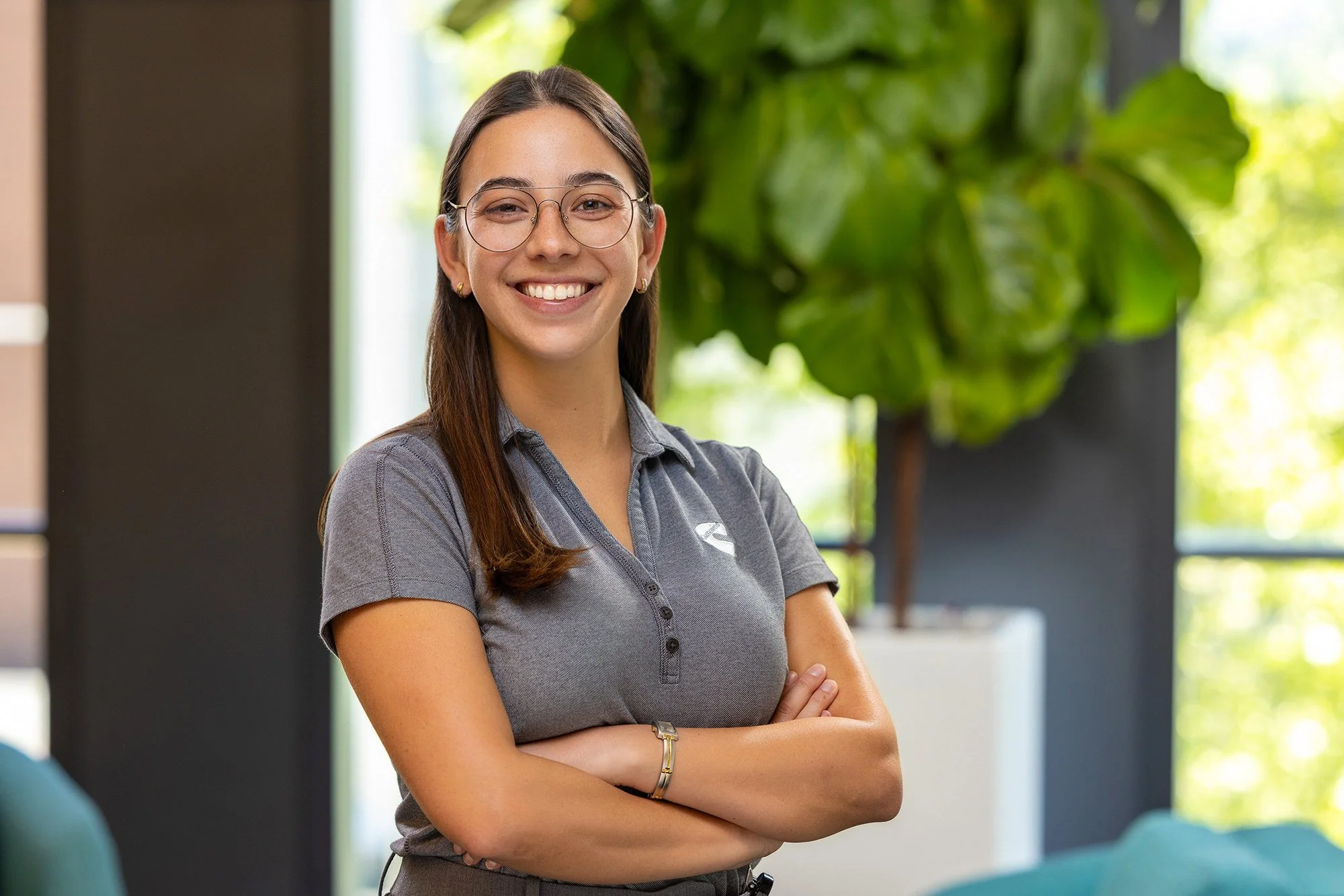Smiling young woman with arms crossed in front of greenery, Cummins employee portrait