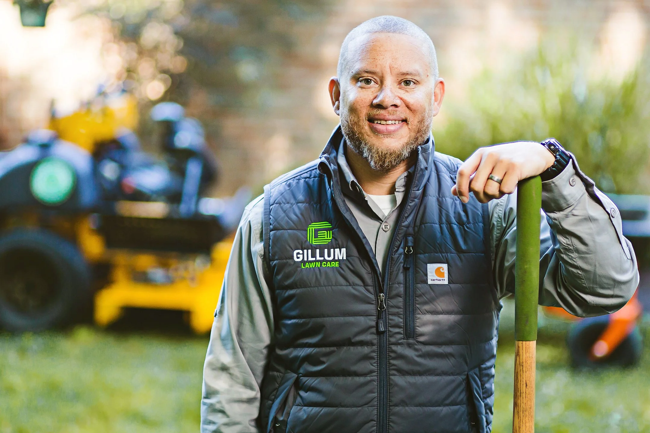 Lawn care business owner leaning on a tool beside a commercial mower, branding portrait in Indianapolis