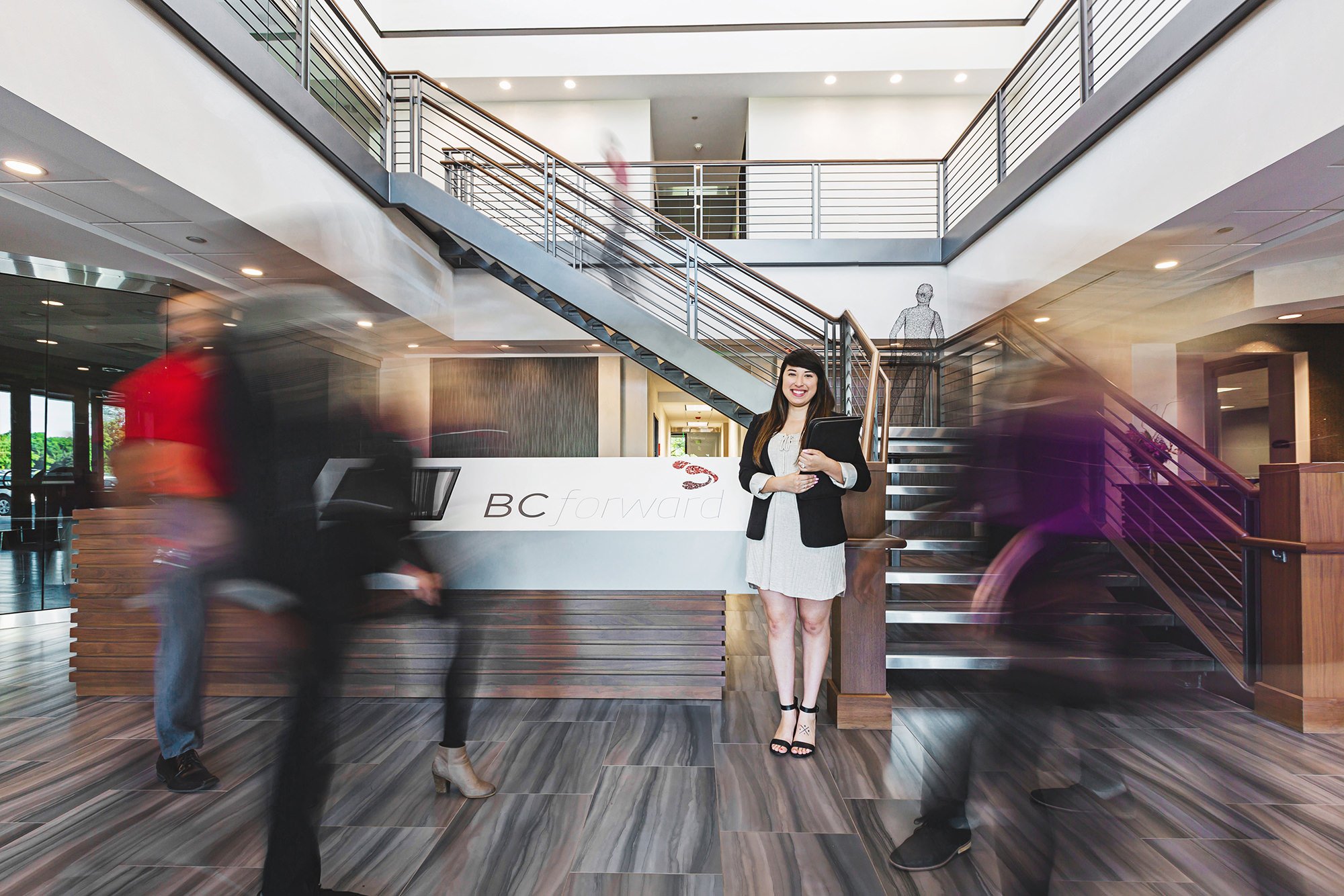 Professionals walking through a modern two-story office lobby, BCforward brand photography