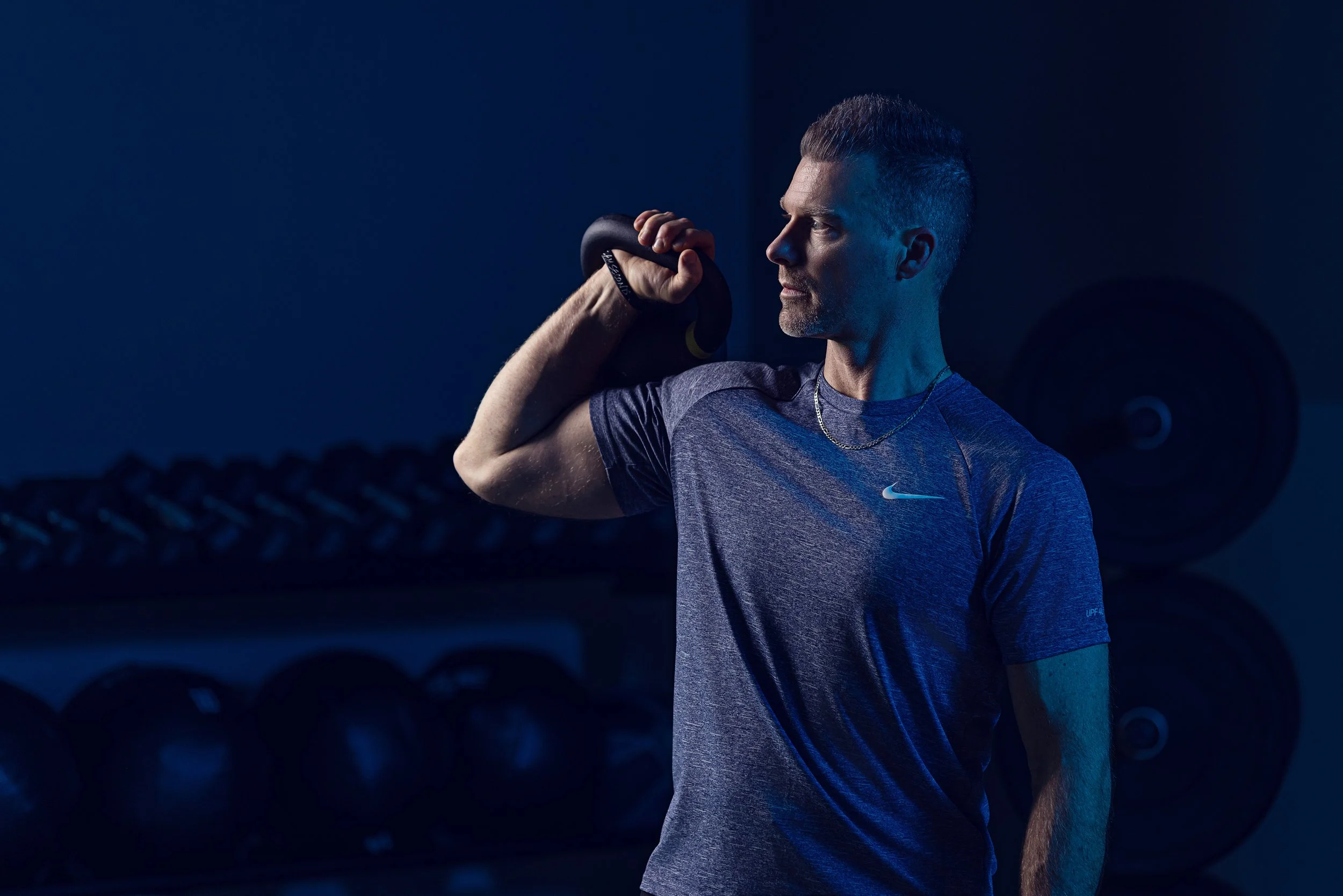 Fitness professional lifting a kettlebell in a dark, blue-lit gym, Indianapolis branding portrait