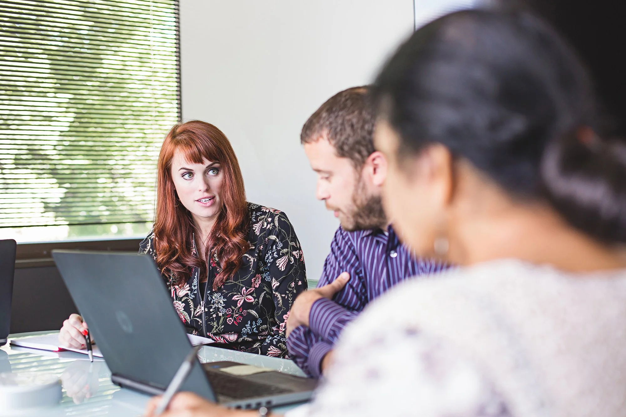 Coworkers collaborating around a laptop in a meeting room, BCforward brand photography