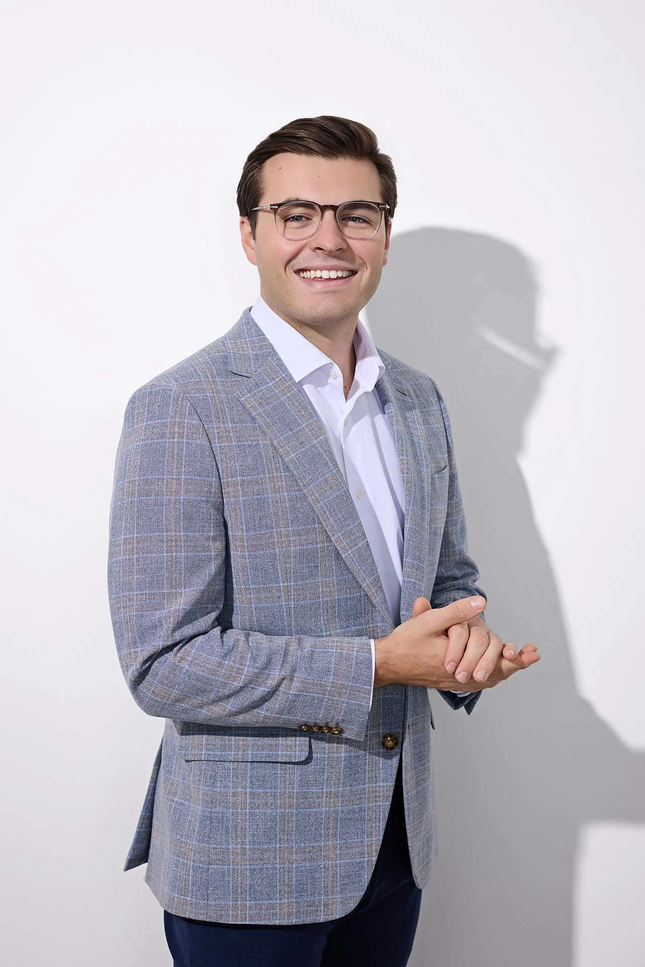 Smiling businessman in a gray plaid blazer against a white studio backdrop, personal branding headshot