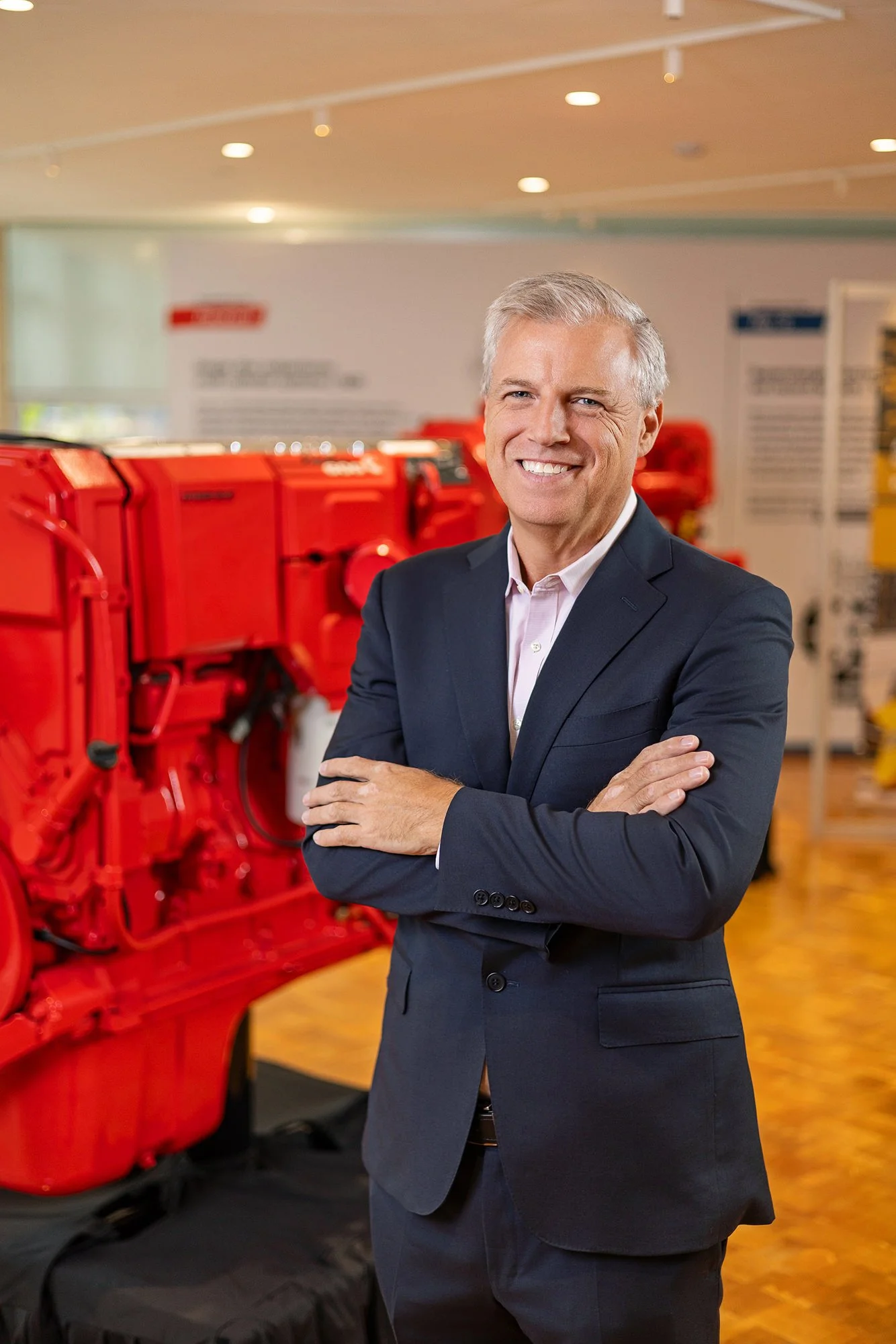 Smiling executive standing in front of a red Cummins engine, corporate portrait in Indianapolis