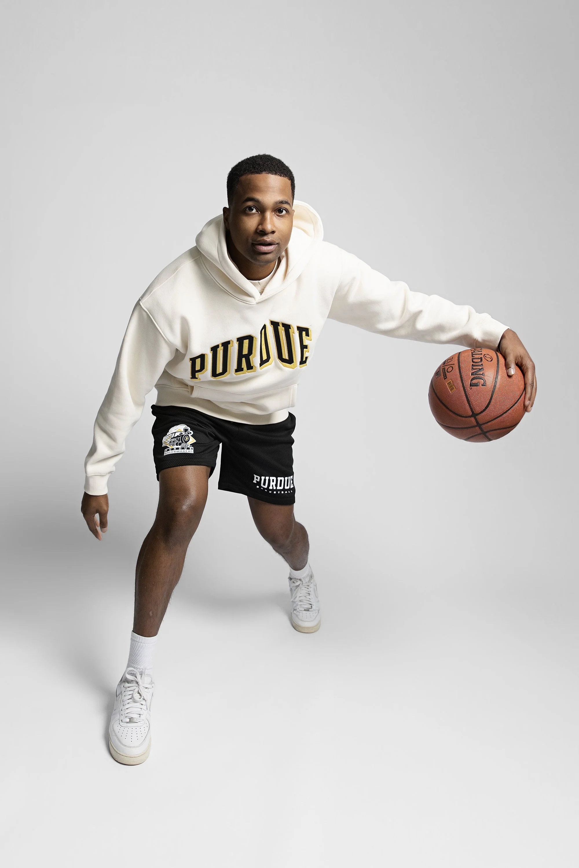 Model dribbling a basketball in a cream Purdue hoodie and shorts, Homefield Apparel studio photo in Fishers