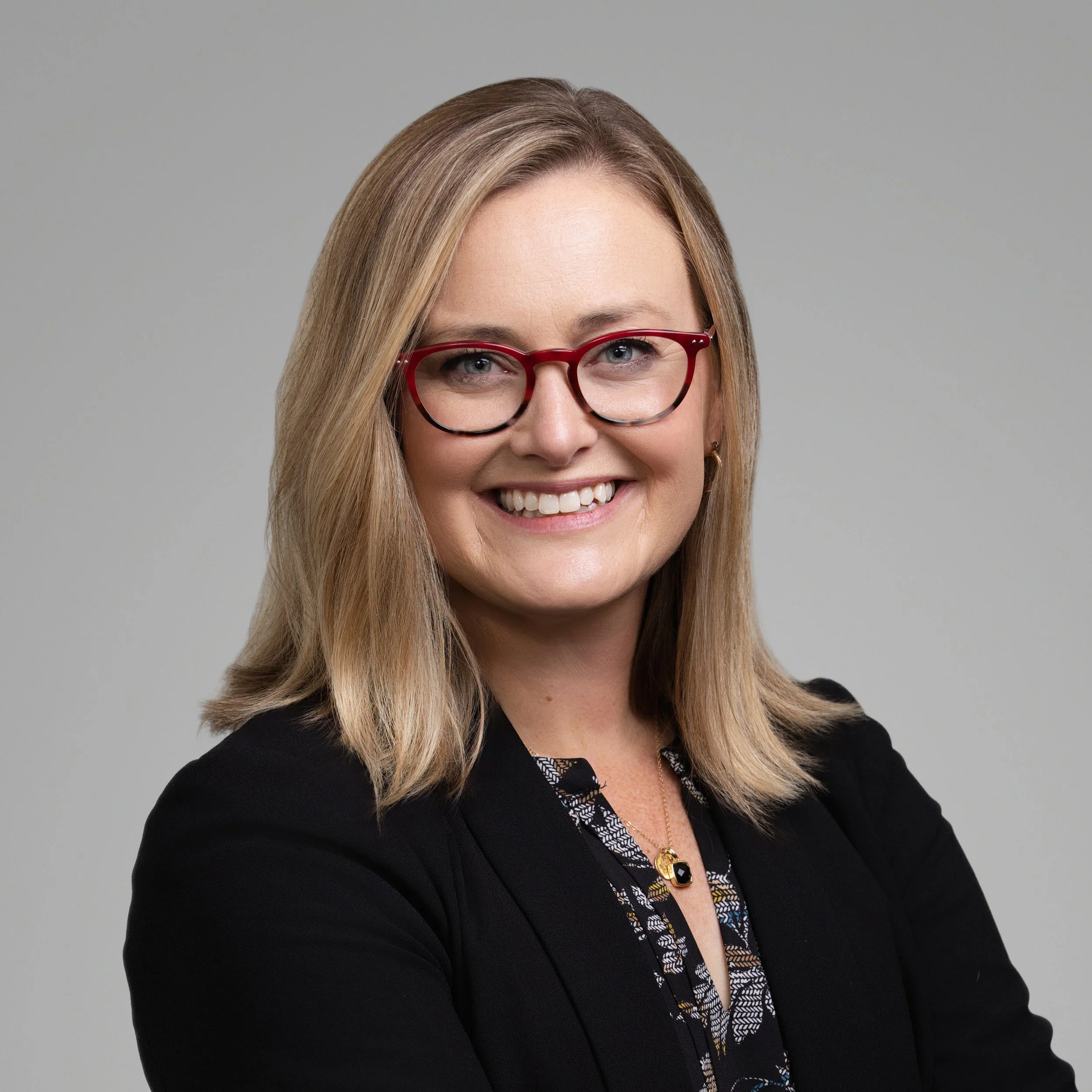 Smiling blonde woman in red glasses and a black blazer, professional headshot in Fishers, Indiana