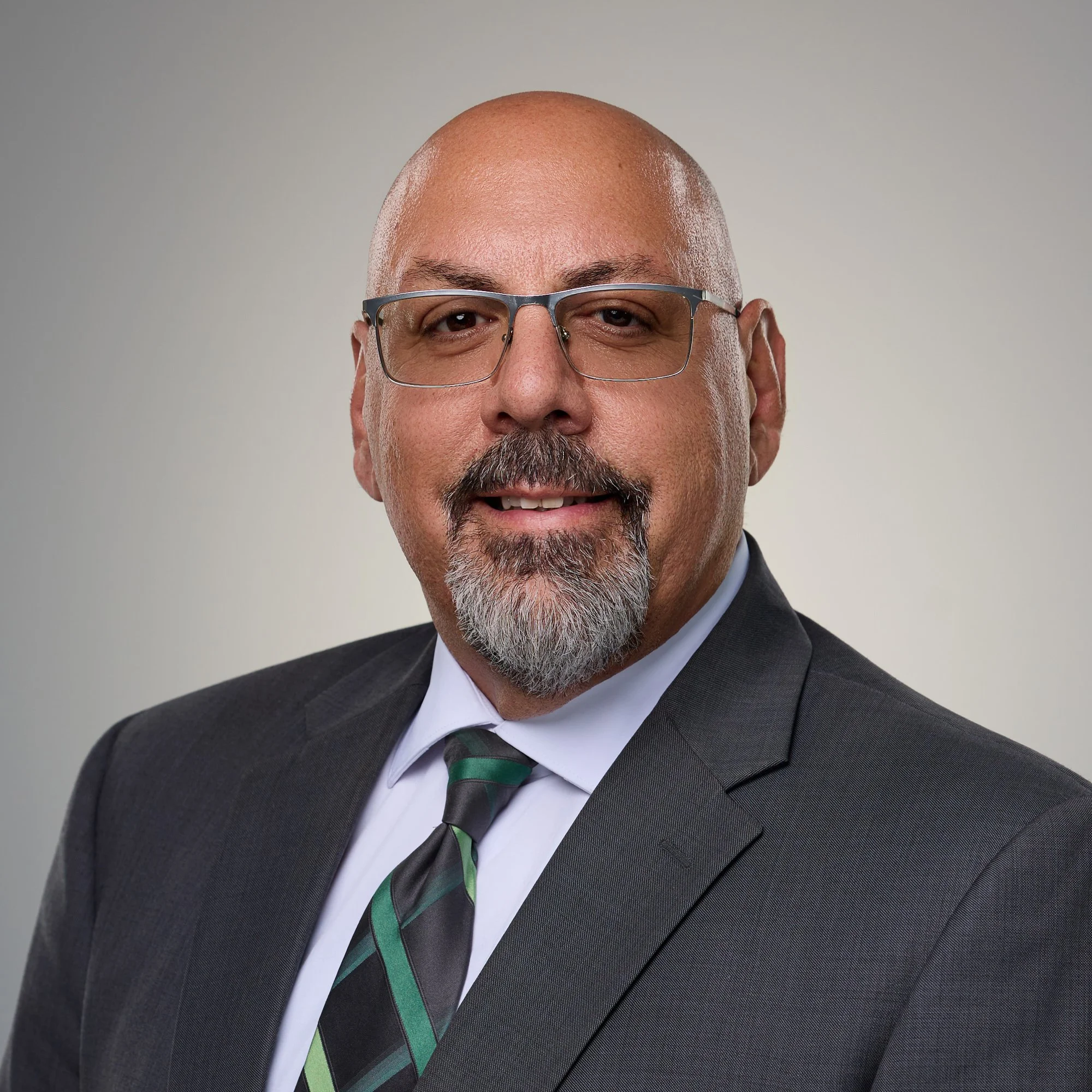 Smiling bald man with a goatee in a gray suit and green tie, business headshot in Fishers