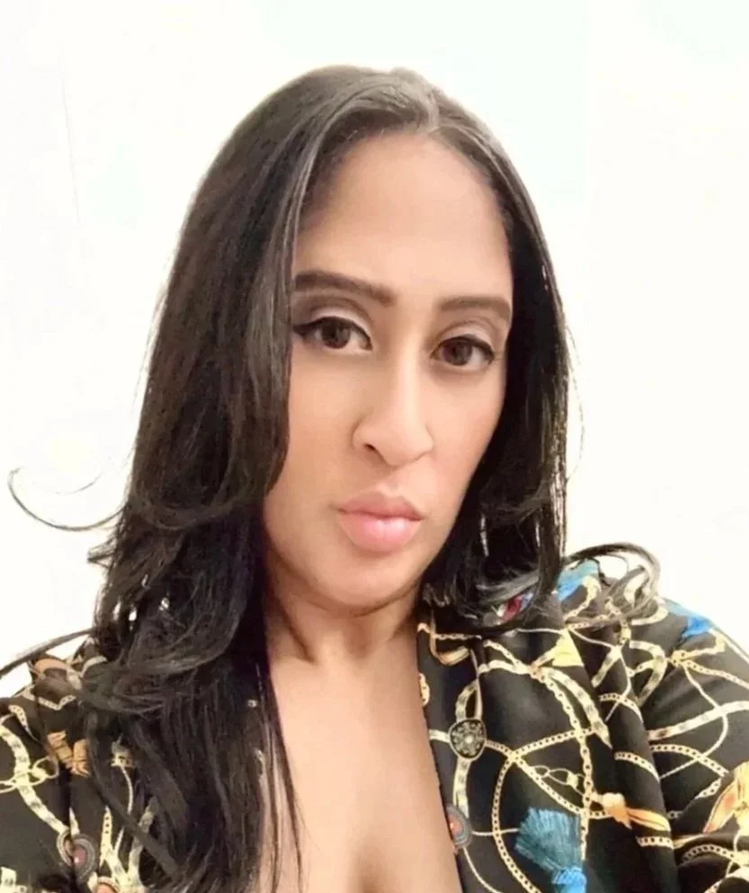 A woman with long dark hair taking a selfie against a plain white background.