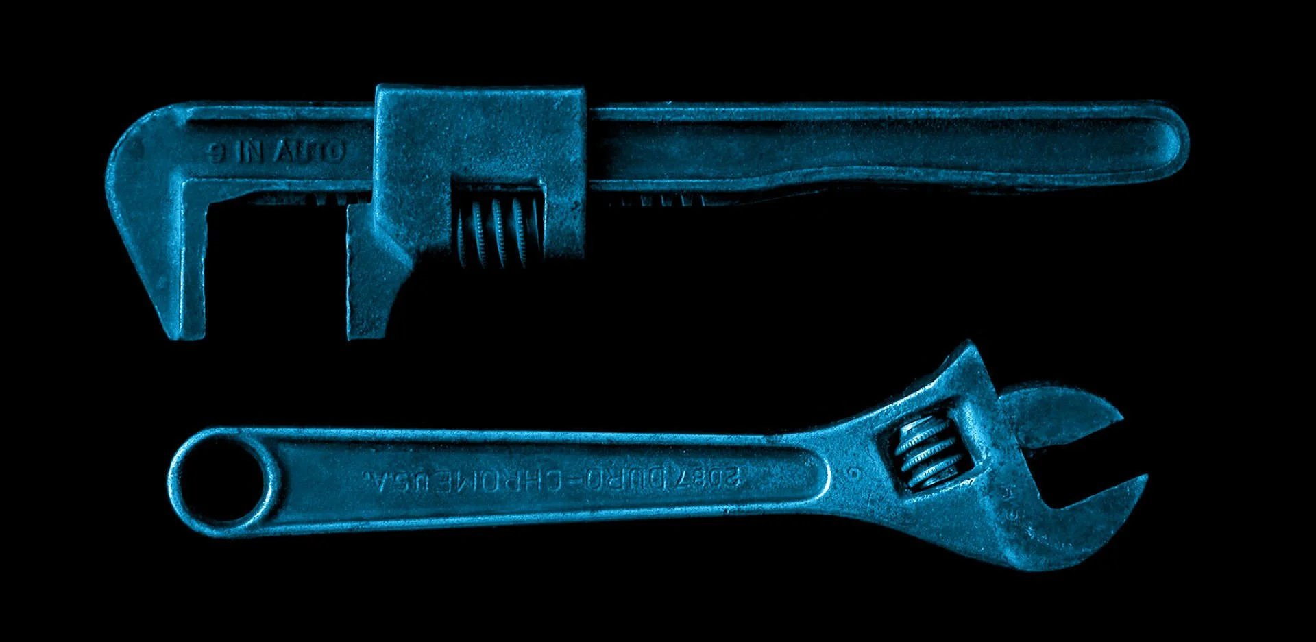 Deux clés, une clé à molette et une clé anglaise, colorées en bleu, disposées horizontalement sur un fond noir.