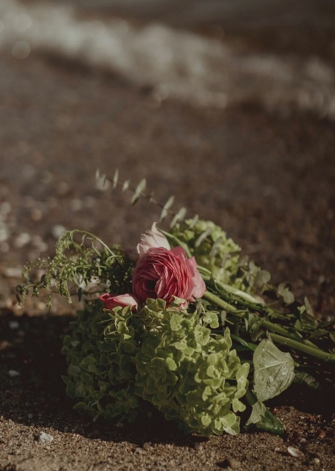 A bouquet of pink and green flowers lying on the sandy ground.