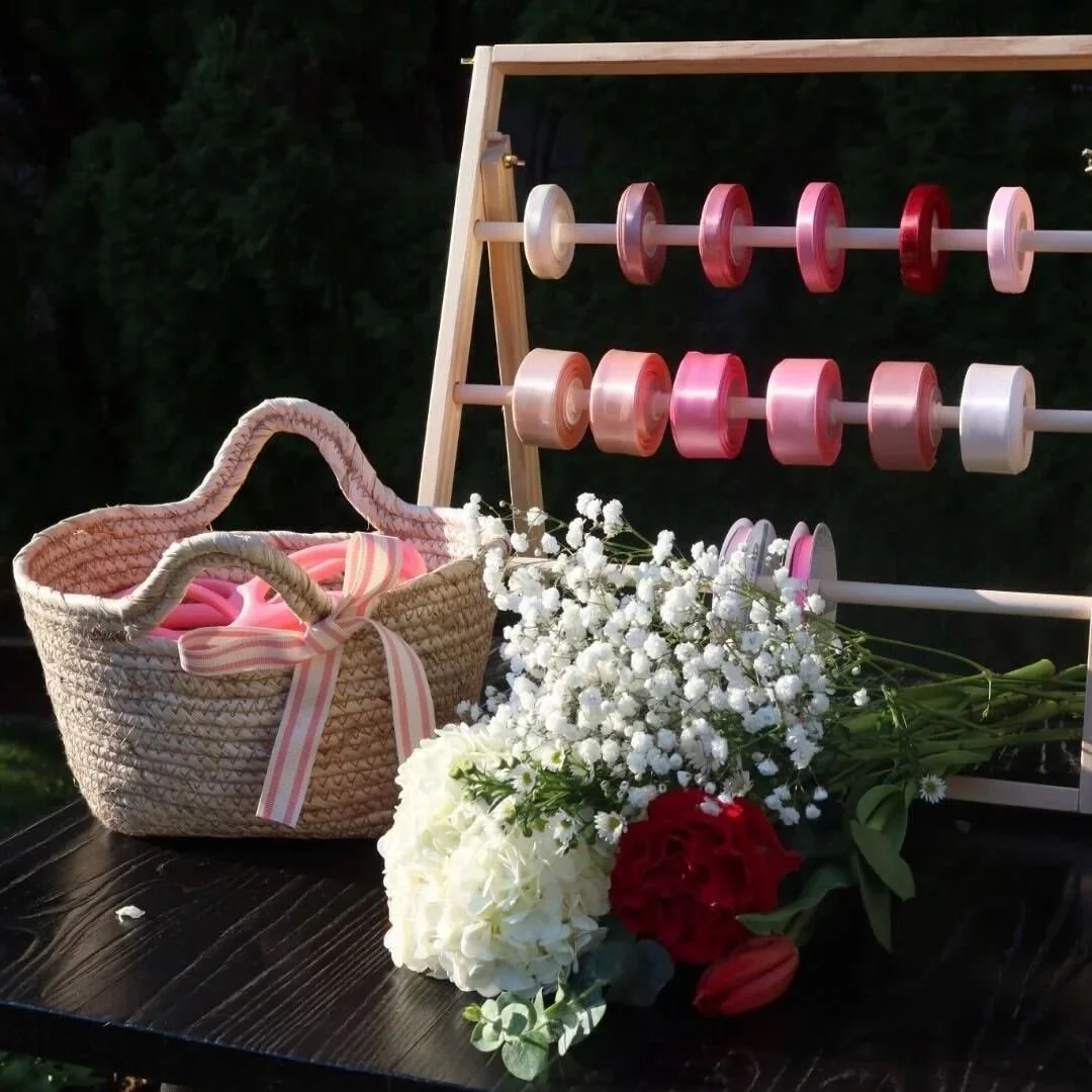 A black table with a basket filled with pink ribbon, a bunch of white and red flowers, and a wooden pegboard with pink and white spool-like objects