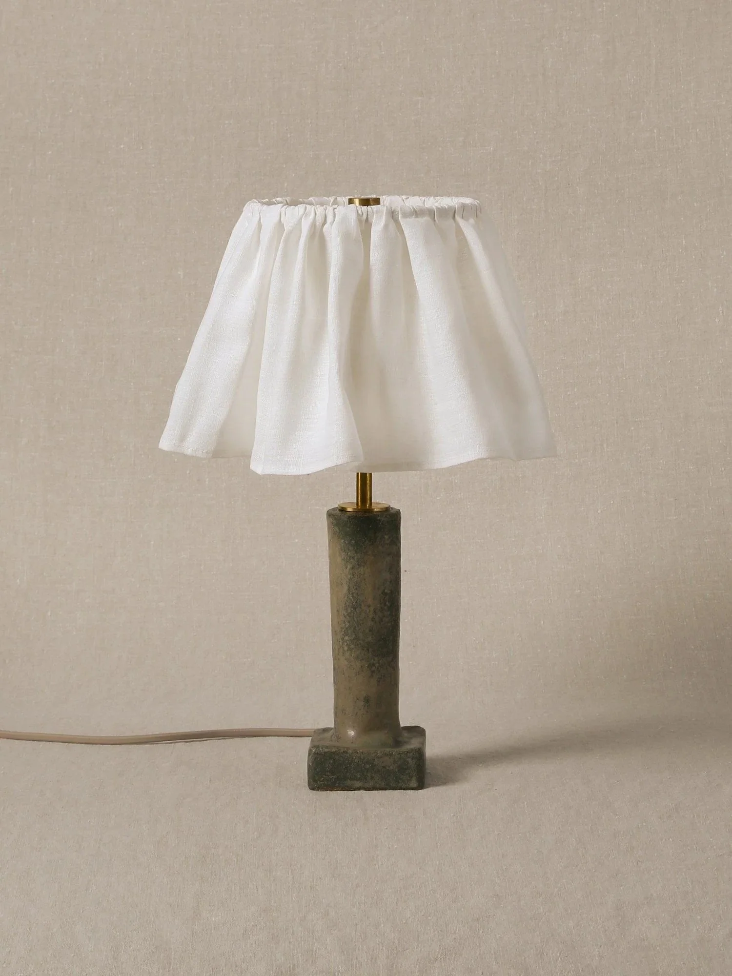 A stone base with a brass pole and a white fabric lampshade on top, set against a plain neutral background.