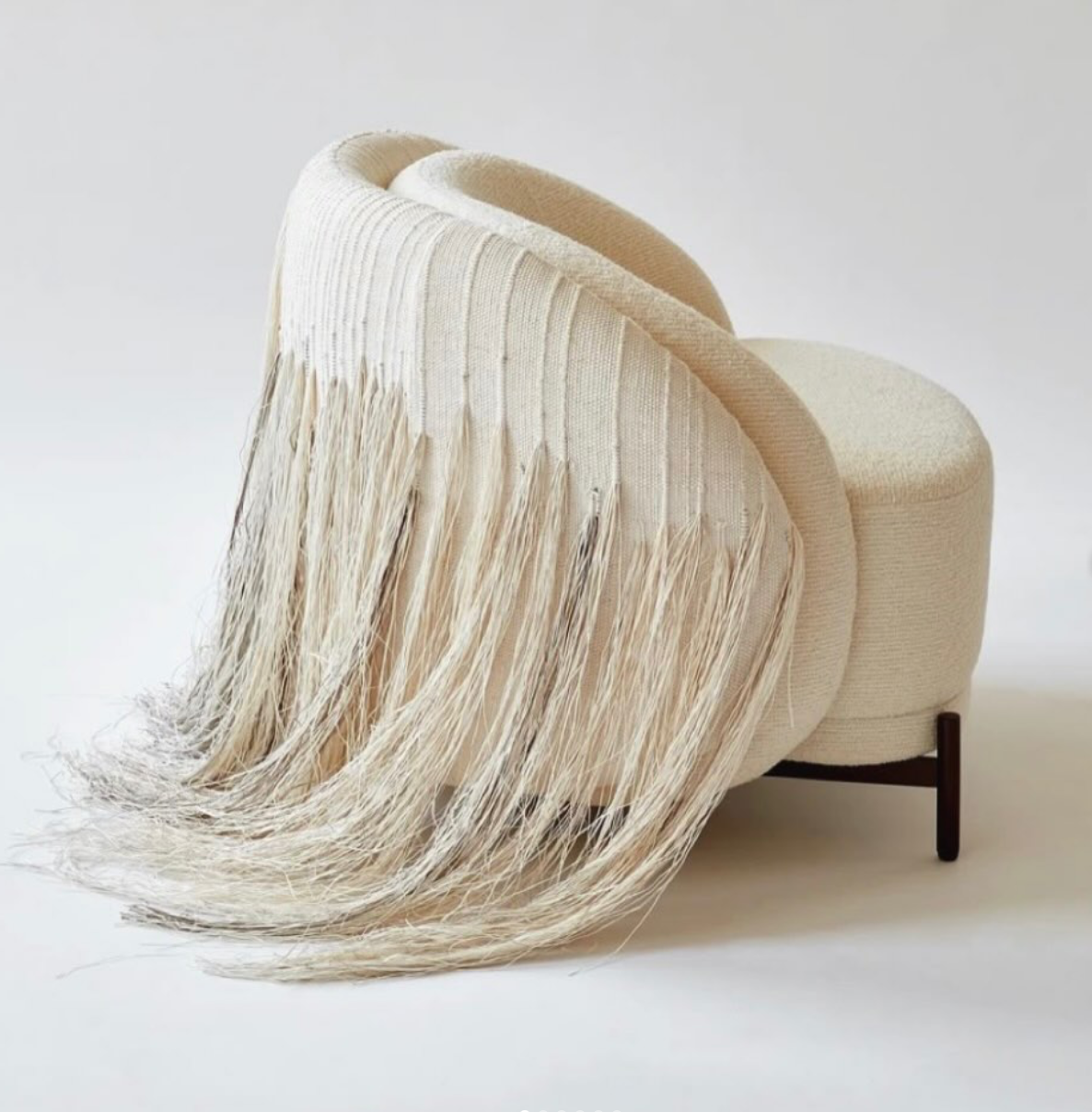 A modern, beige chair with fringed upholstery draped over it, set against a plain white background.