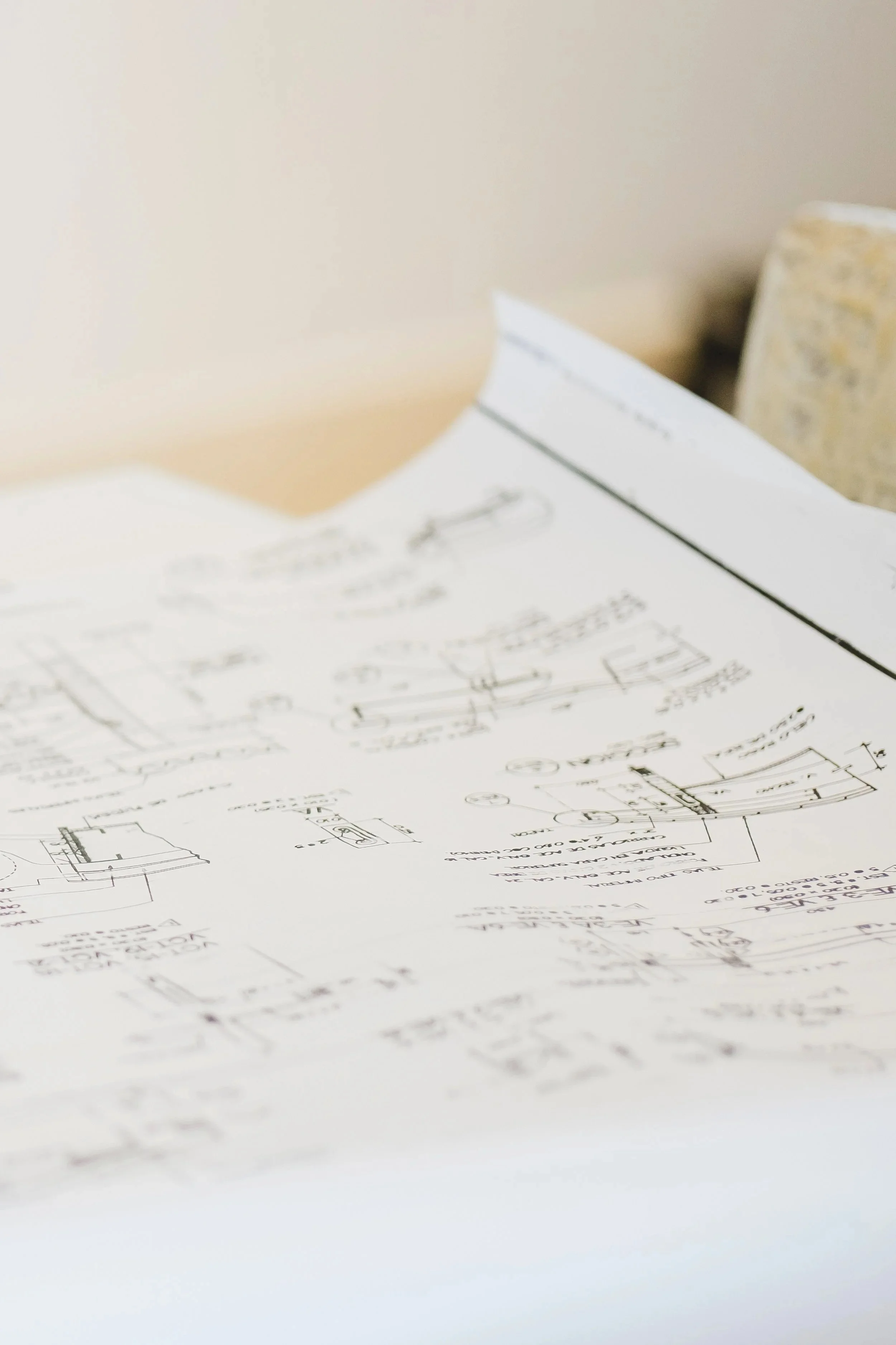 Architectural blueprint plans on a white table, with a beige wall in the background.
