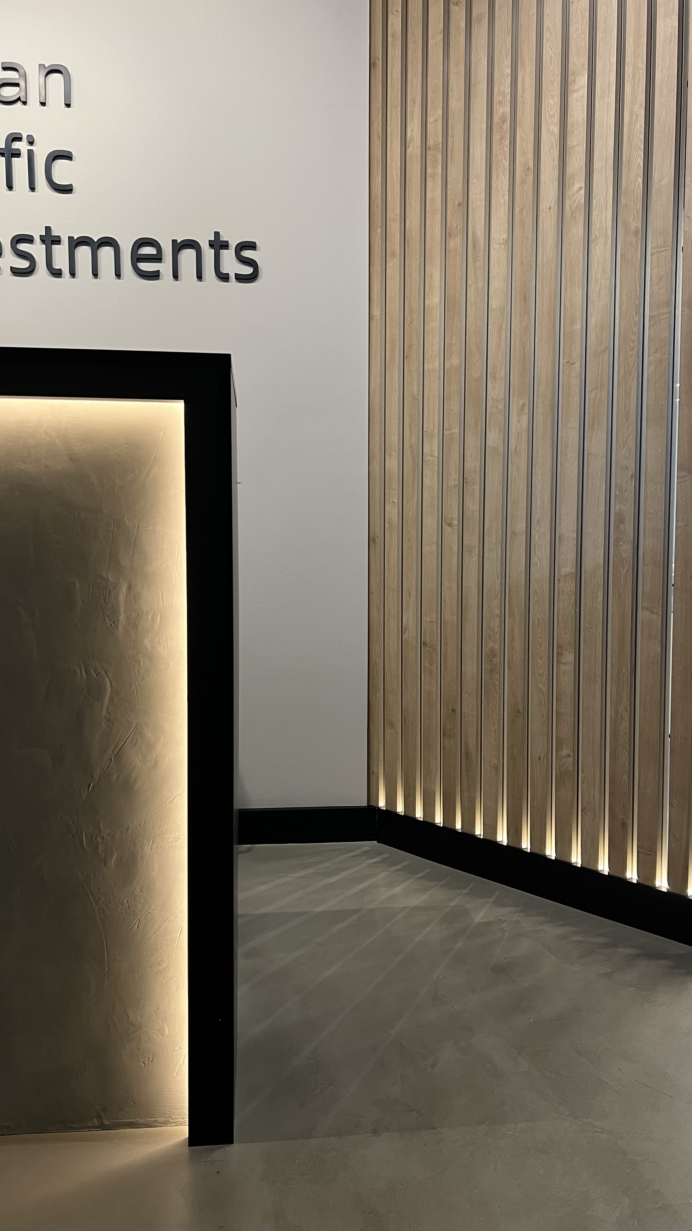 Interior of a building with a white wall, partial black fireplace, and wooden slat wall with lighting at the base.