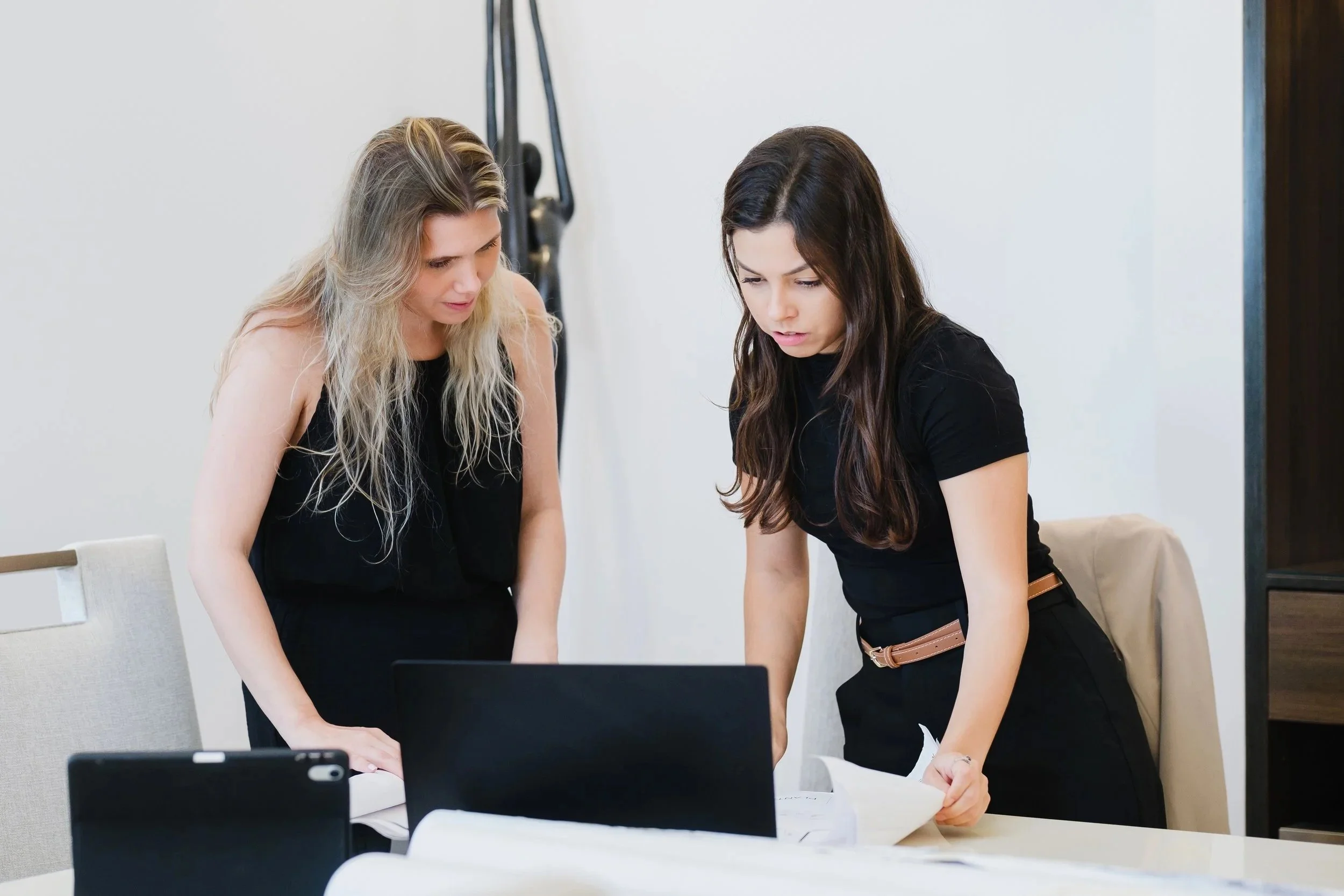 Two women are looking down at documents on a table in a meeting room.
