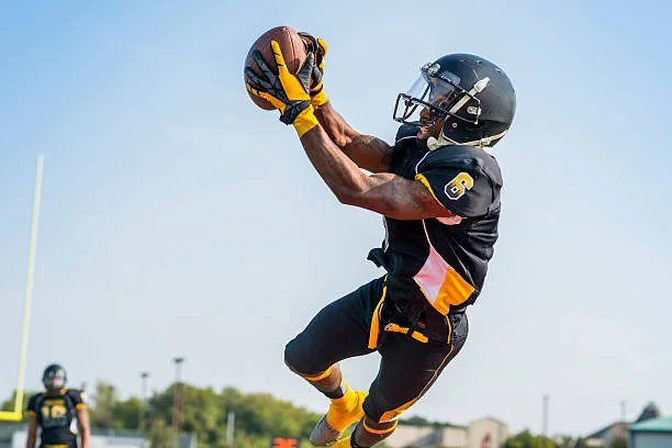 A football player in black and yellow uniform catching a football mid-air during a game.