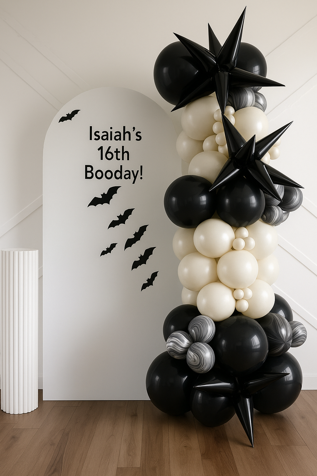 Black, white, and gray balloons arranged as a Halloween-themed birthday decoration, with a white backdrop that reads "Isaiah's 16th Booday!" and black bat silhouettes.