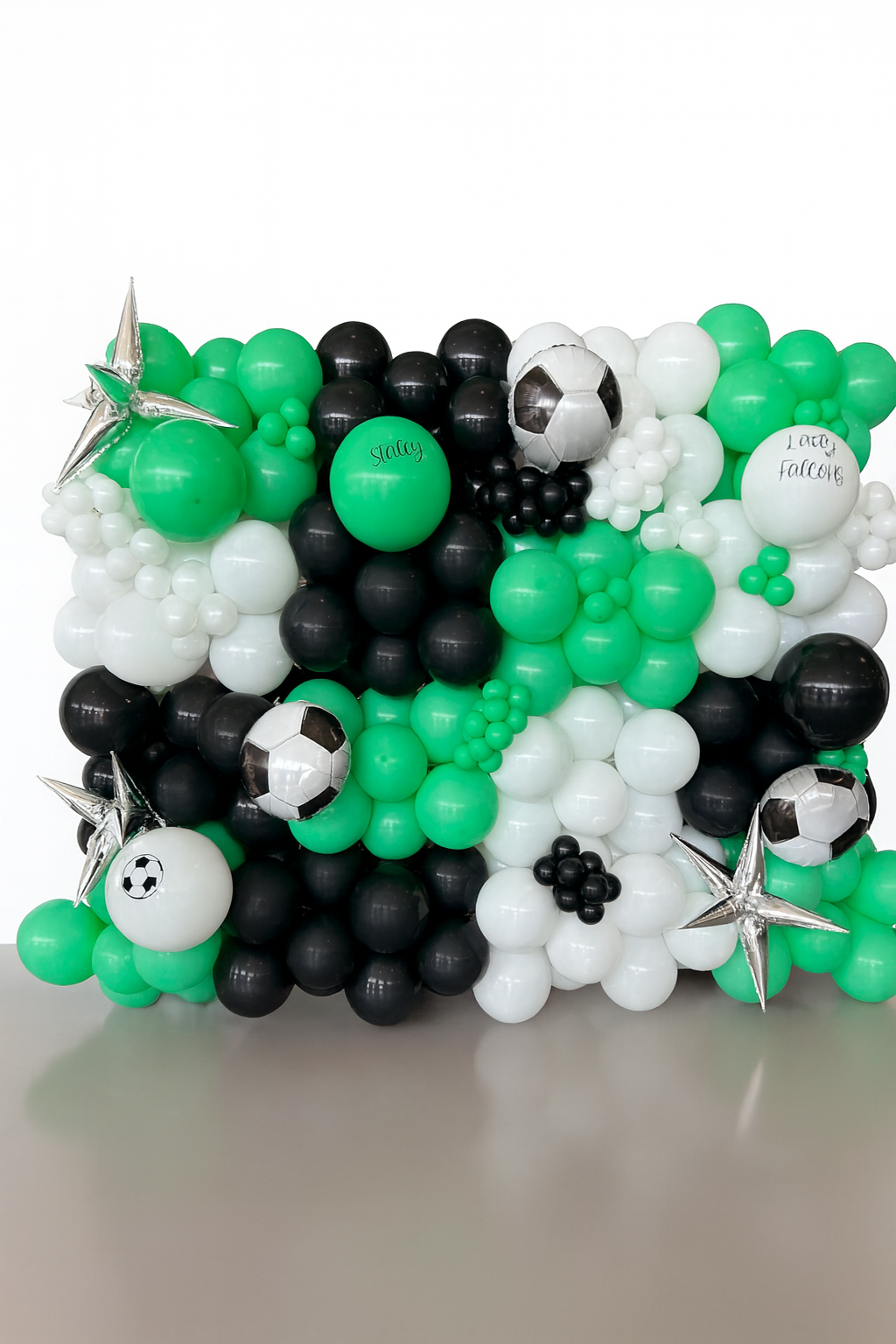 Balloon arrangement with soccer balls, stars, and green, black, and white balloons, some with handwritten messages.