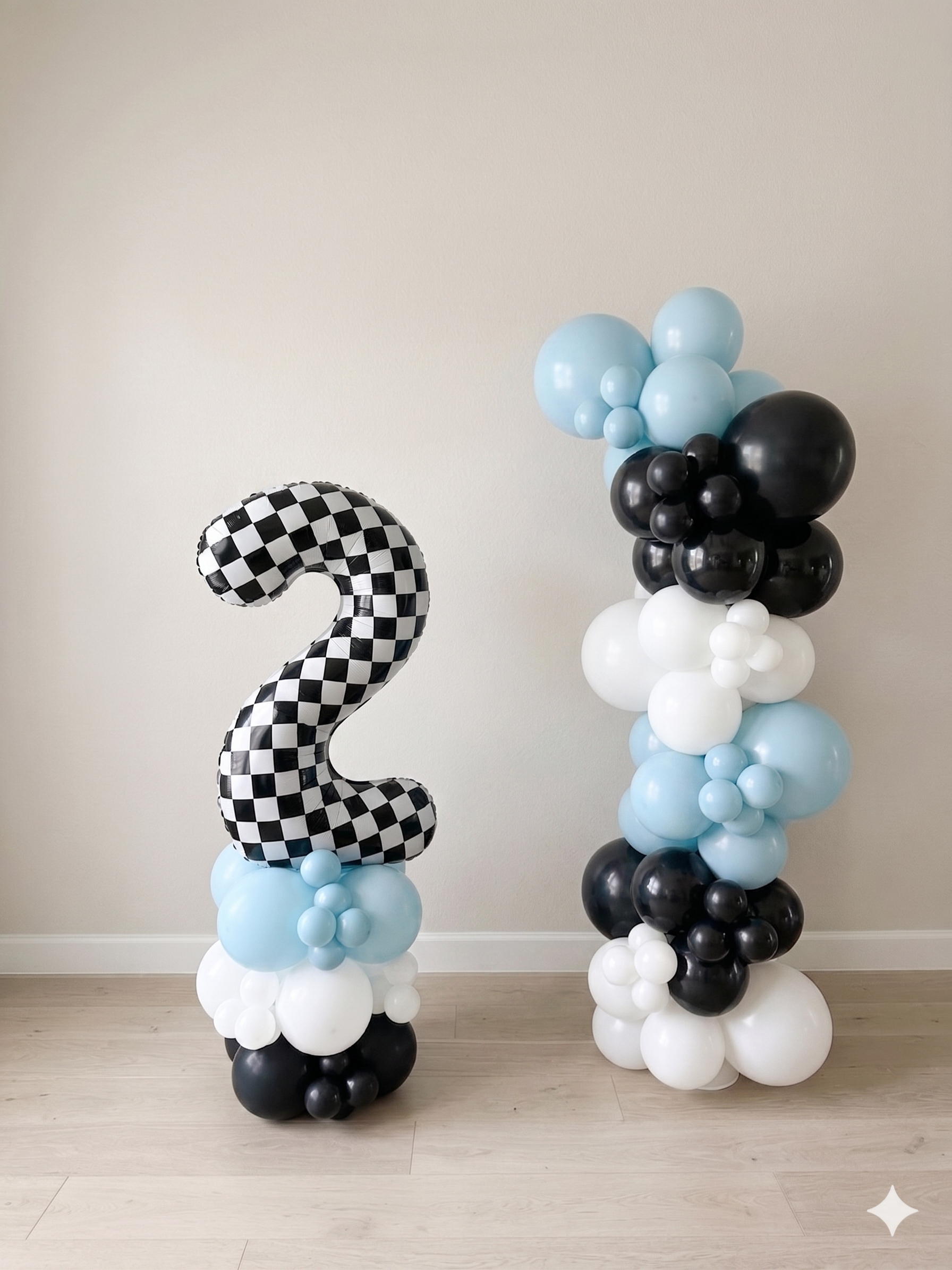 Two balloon arrangements, one with a checkered number 2 balloon and the other with black, white, and light blue balloons, against a plain white wall.