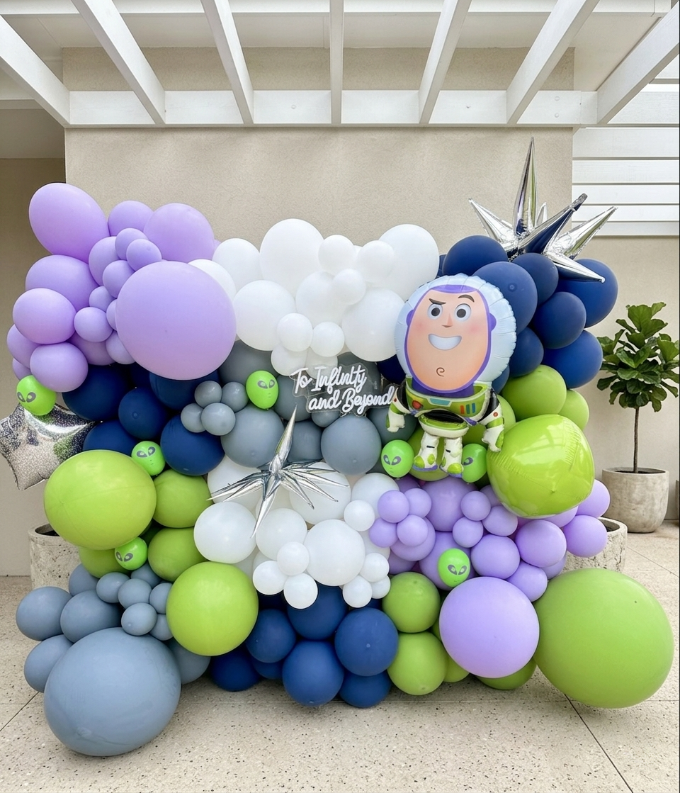 Galaxy-themed balloon arrangement featuring purple, white, green, and blue balloons, with a Buzz Lightyear balloon and silver star-shaped balloons, and a sign that reads 'To Infinity and Beyond!'
