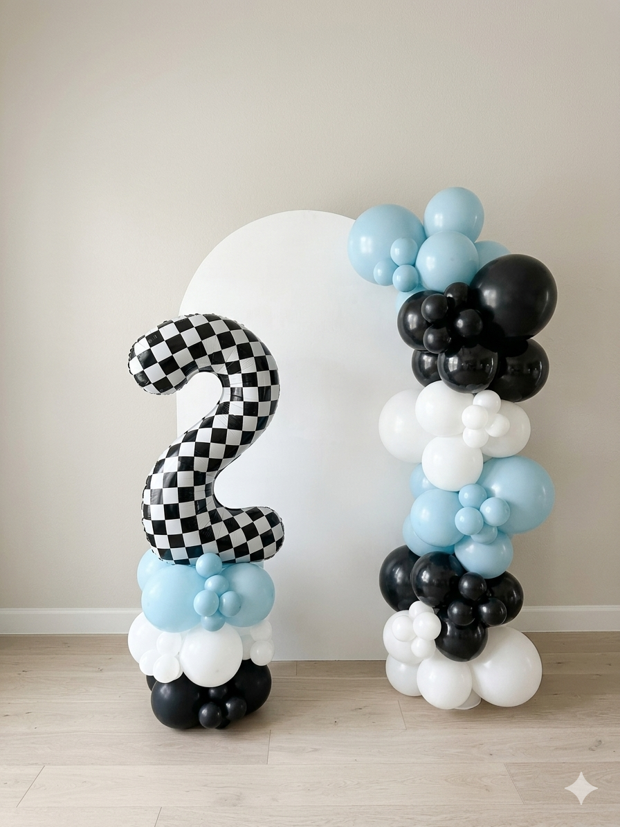 Balloon arrangement with a large checkered number 2 balloon, surrounded by clusters of black, white, and light blue balloons against a plain wall and wooden floor.