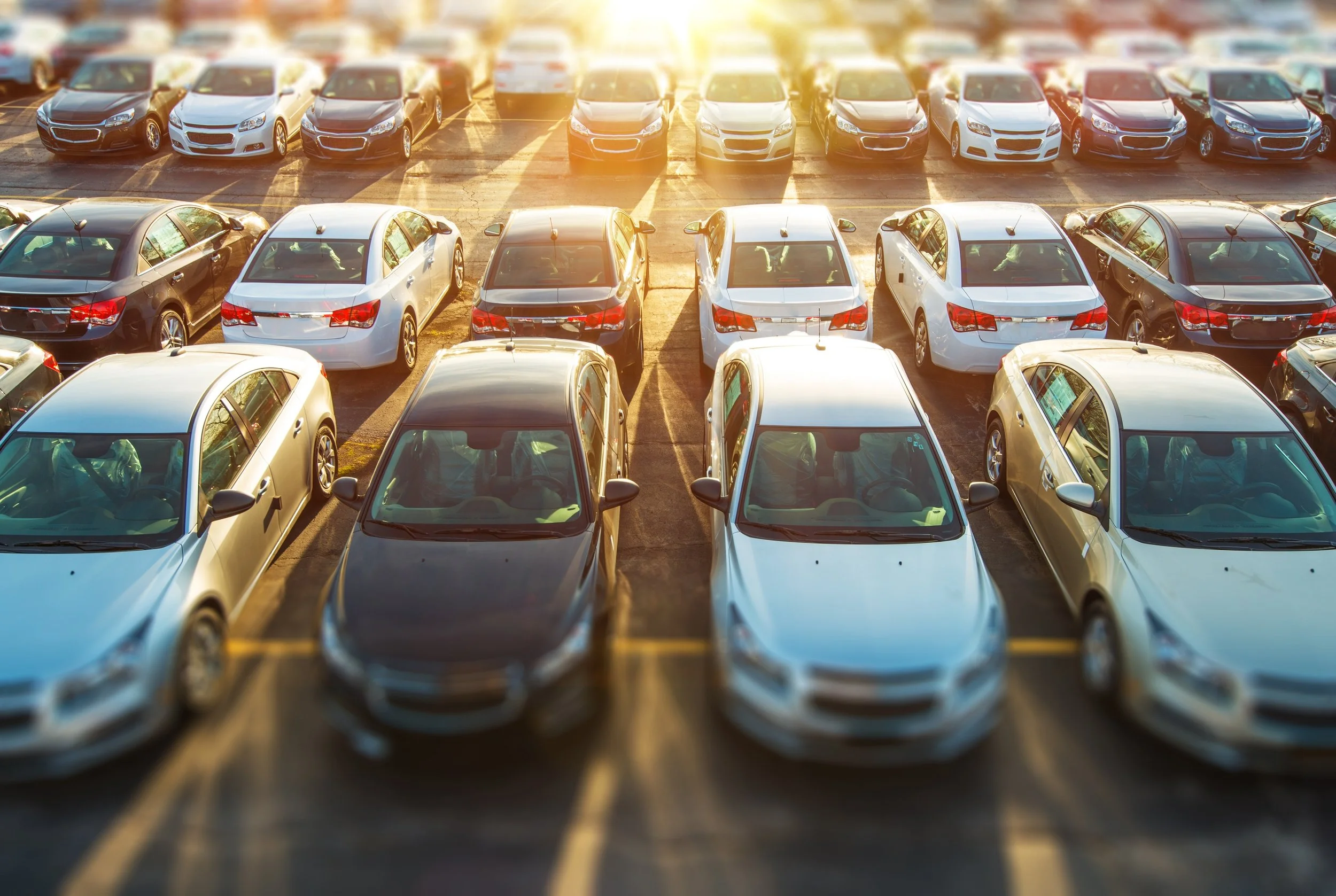 Multiple cars parked in a parking lot with sunlight shining on them.