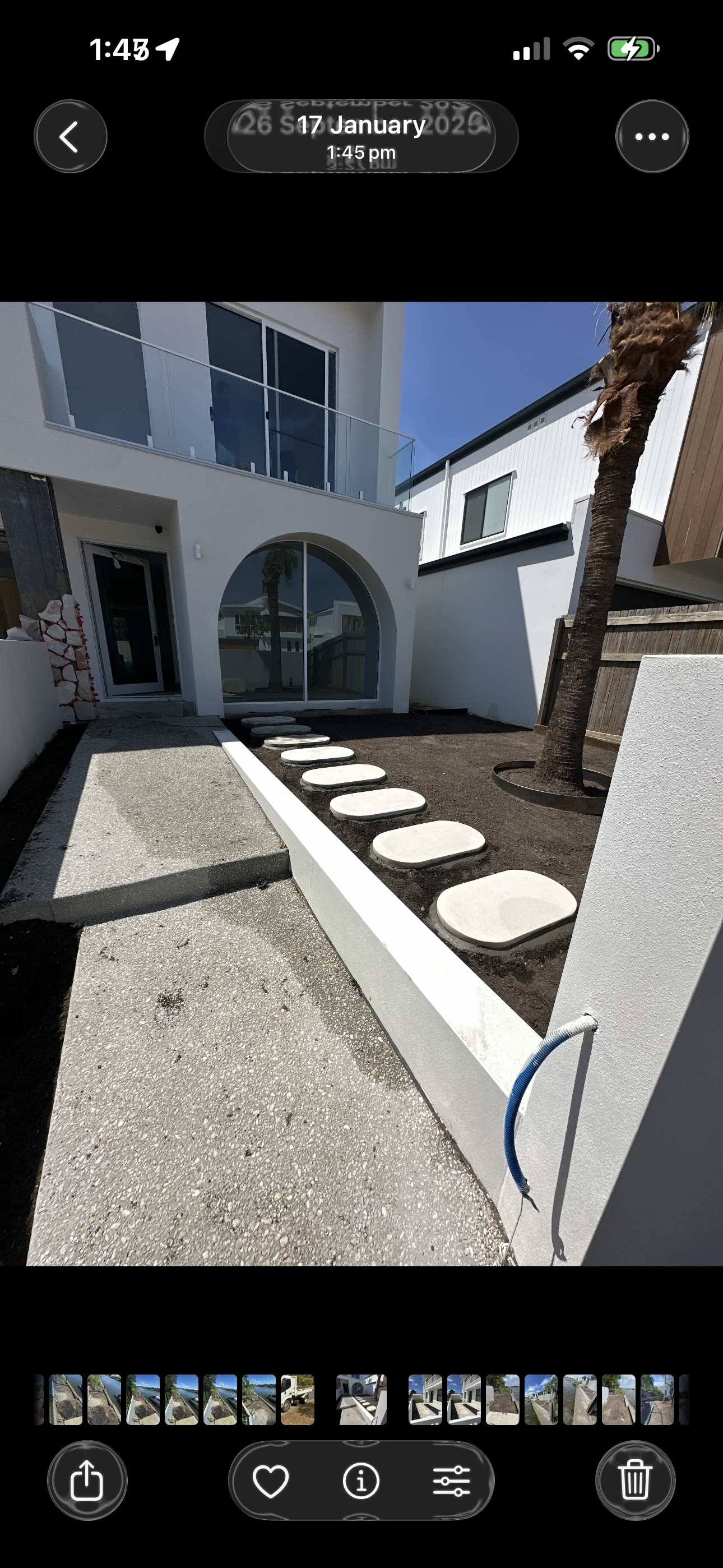 Modern house exterior with a front yard featuring stepping stones, palm tree, and newly landscaped soil, with a balcony and large window visible.