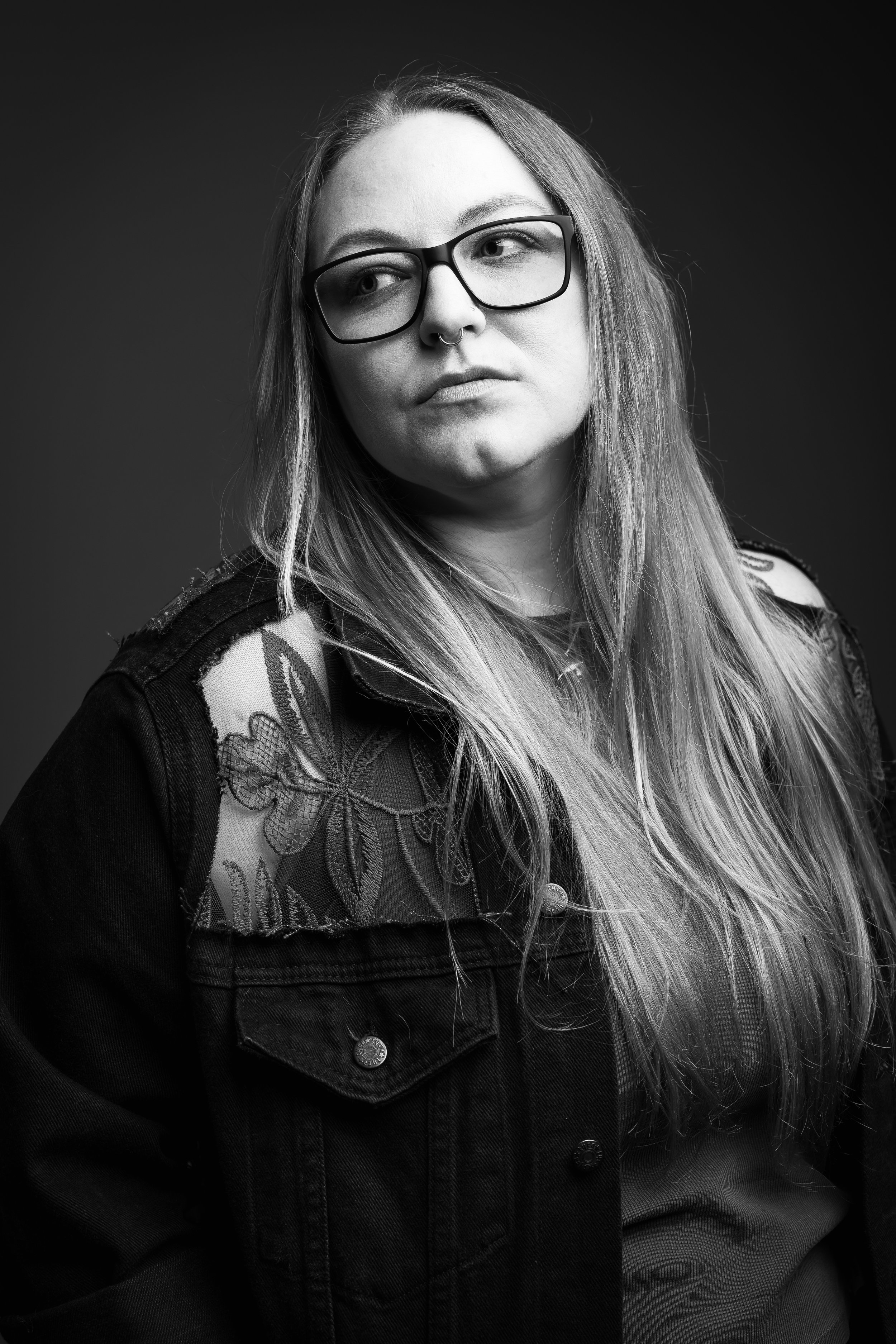 Black-and-white portrait of a woman with glasses and long hair, looking off to the side with a thoughtful expression.   Image by Adrianne Mathiowetz Photography