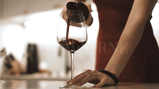 Person pouring red wine into a glass on a countertop.